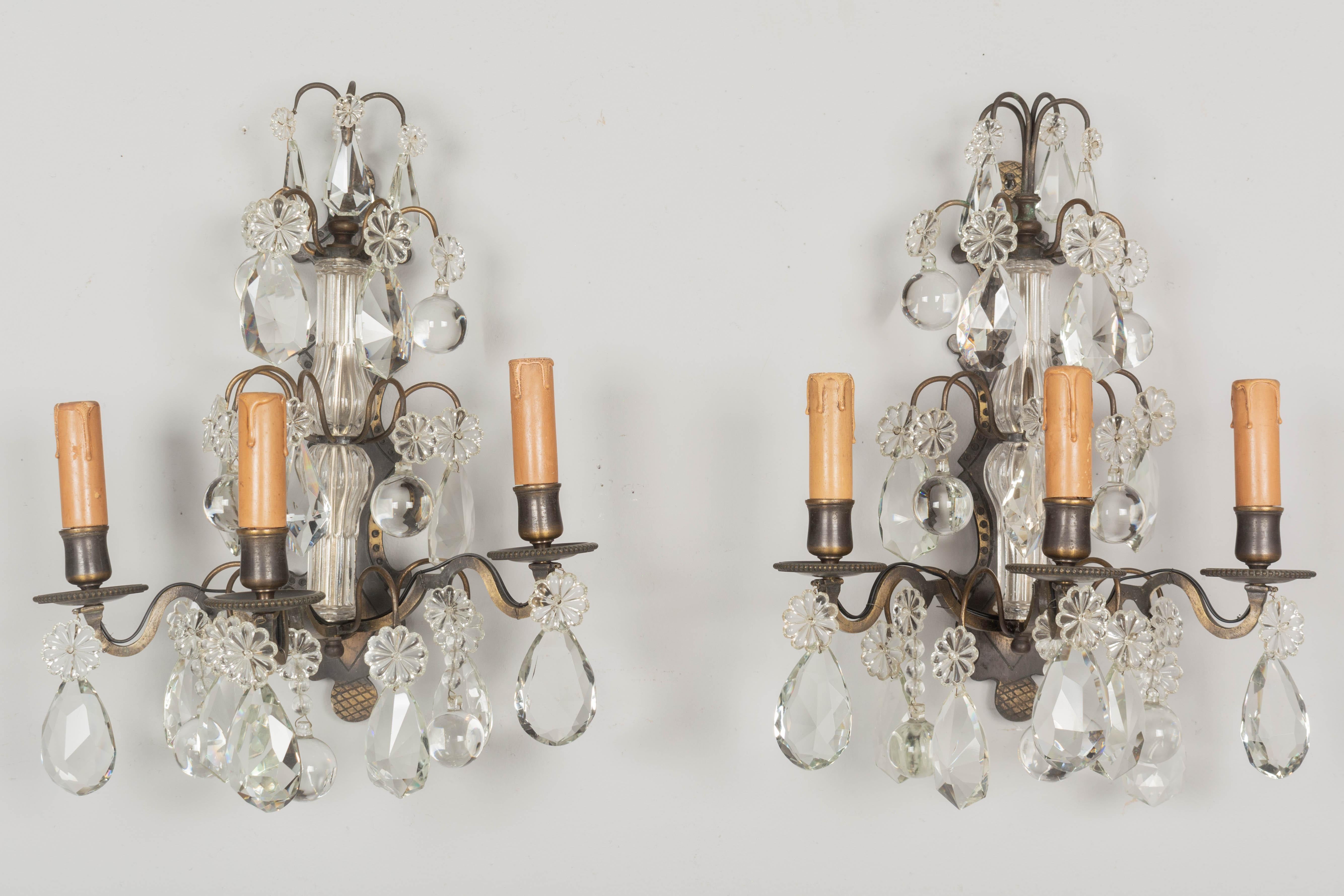 A pair of Louis XV style French Art Deco Period cast brass three light crystal sconces a variety of large cut crystal prisms and pendalogues with rosettes. Good quality heavy casting with dark patina. Rewired using the original sockets with US