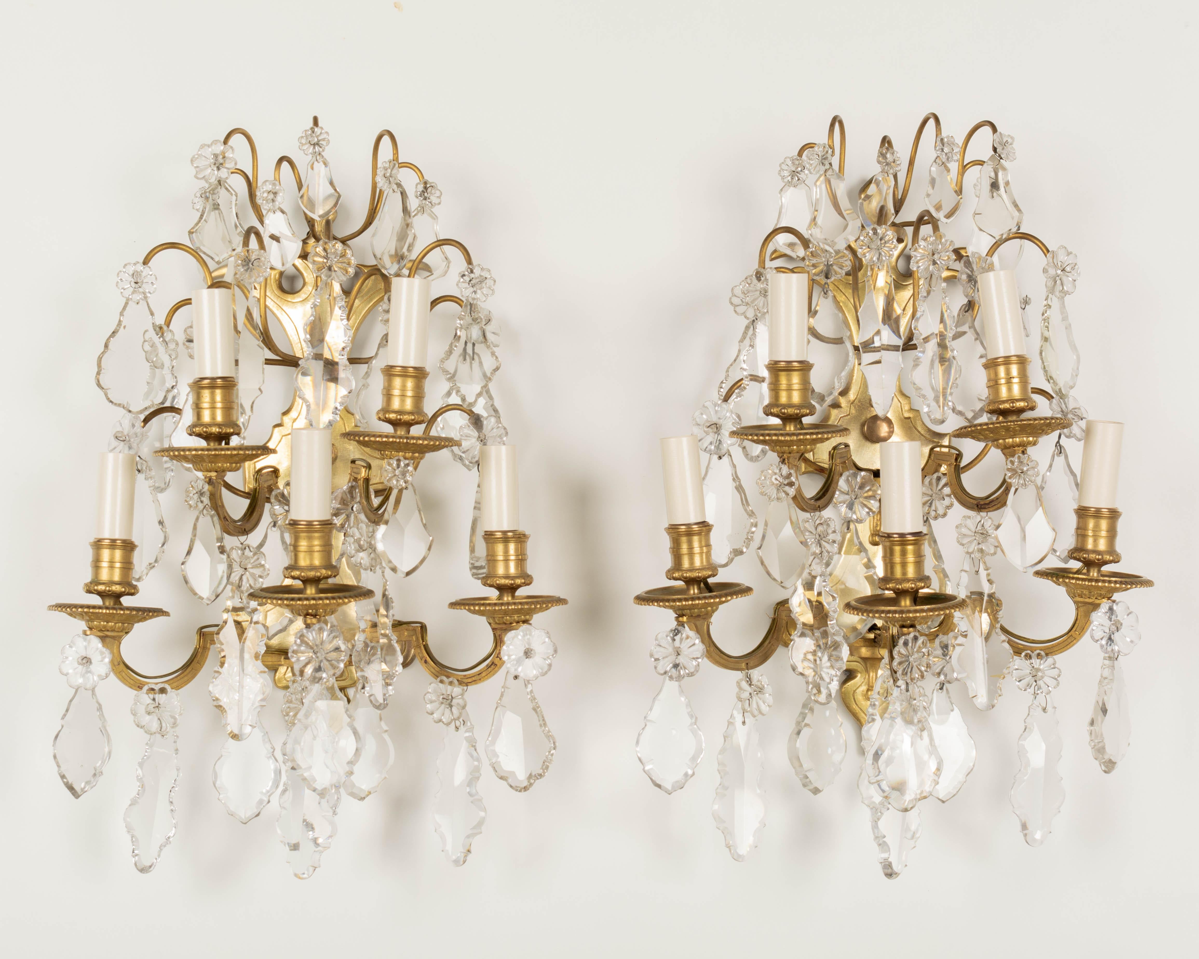 A pair of Louis XV style French Art Deco Period cast bronze and crystal sconces. Good quality heavy casting with five candle lights and a variety of cut crystal prisms and pendalogues. Rewired with new sockets and candle covers.