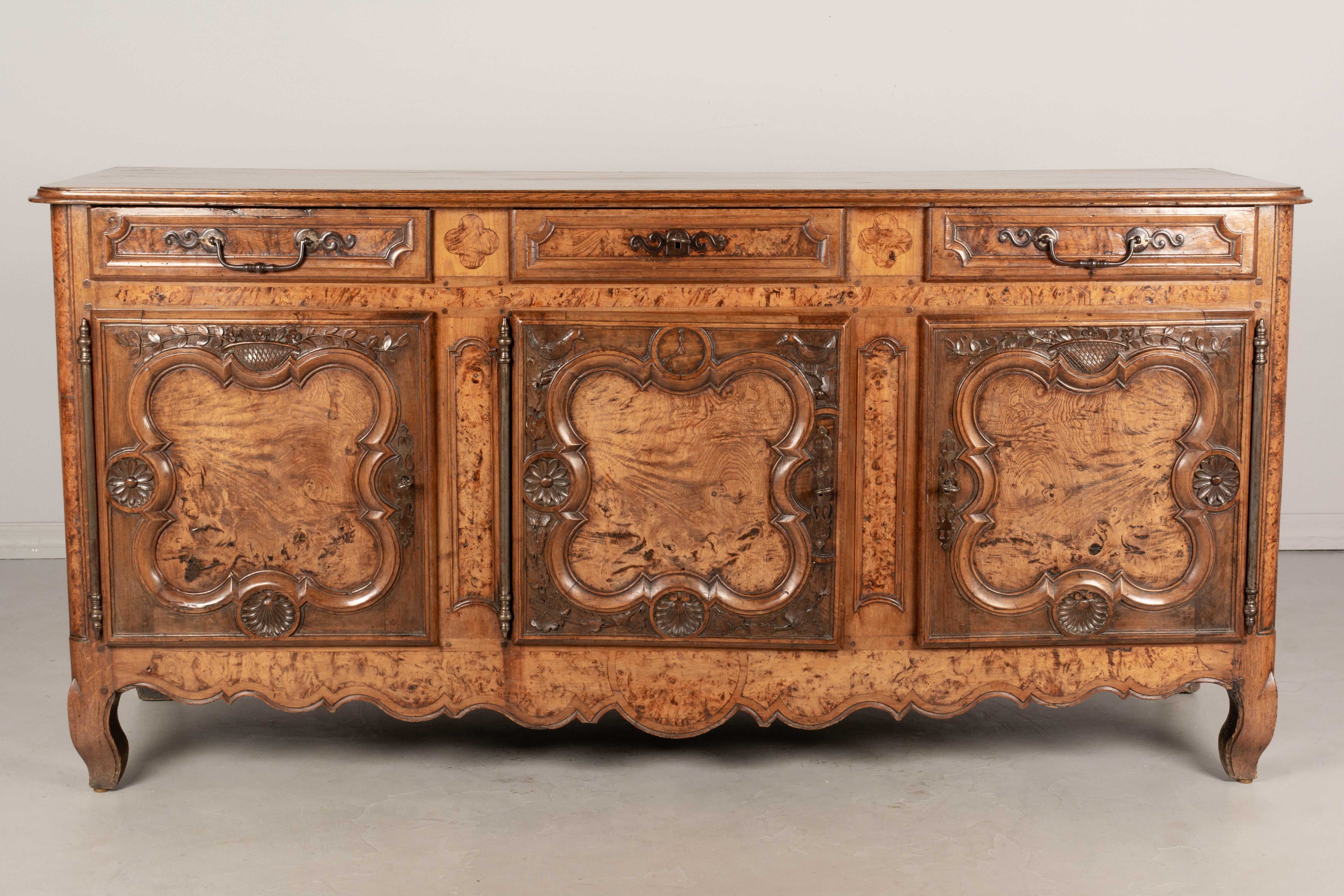 An early 20th century Louis XV style enfilade or sideboard from Burgundy. Made of solid oak and burl of elmwood. Fine hand carvings include a clock on the center door, flower baskets, oak leaves with acorns, a pair of birds, and bold flower and