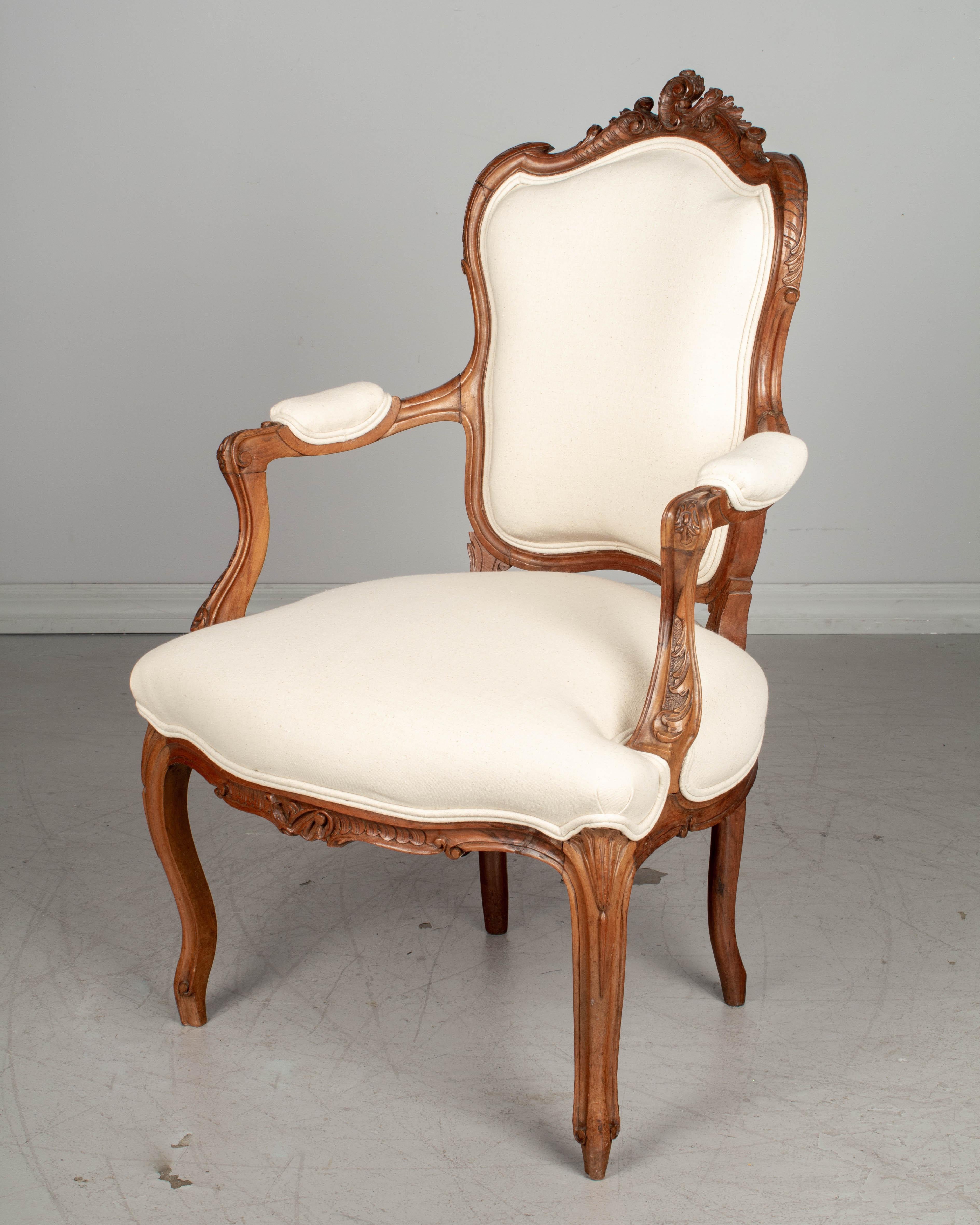 A Louis XV style French fauteuil, or armchair, with sturdy walnut frame and Fine hand carved decoration. Newly upholstered in neutral cotton canvas. This chair sits low to the ground with a seat height of 18