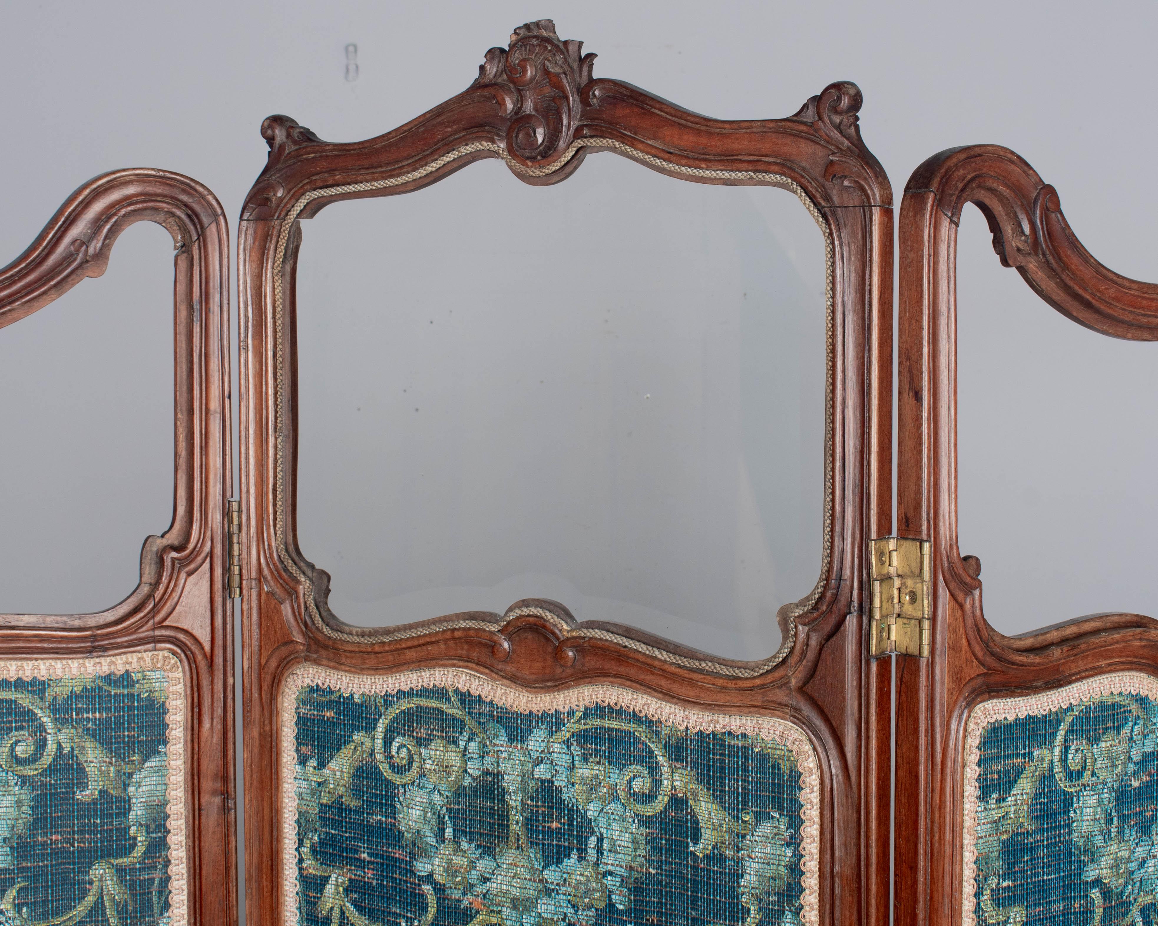 A 19th century French Louis XV paravent, or folding screen, with hand-carved walnut frame. Three hinged panels are each lined on both sides with beautiful teal blue textured wall paper with decorative trim. Top center panel is fitted with beveled