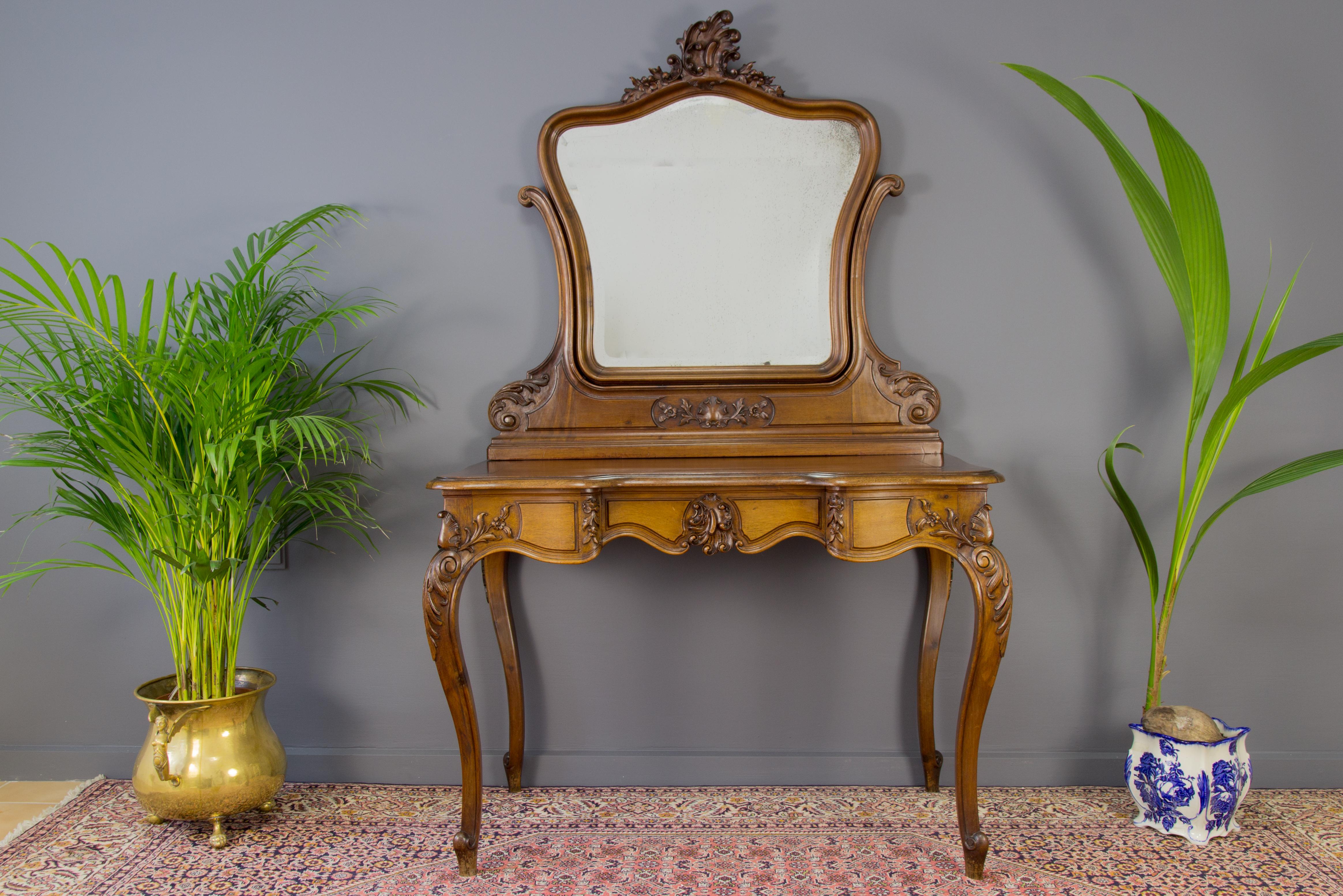 French walnut Louis XV style dressing table or vanity table is beautifully carved throughout with rocaille, foliate and floral motifs, is standing on very elegant cabriole legs. Original beveled mirror with a nice original patina. 
Free delivery in