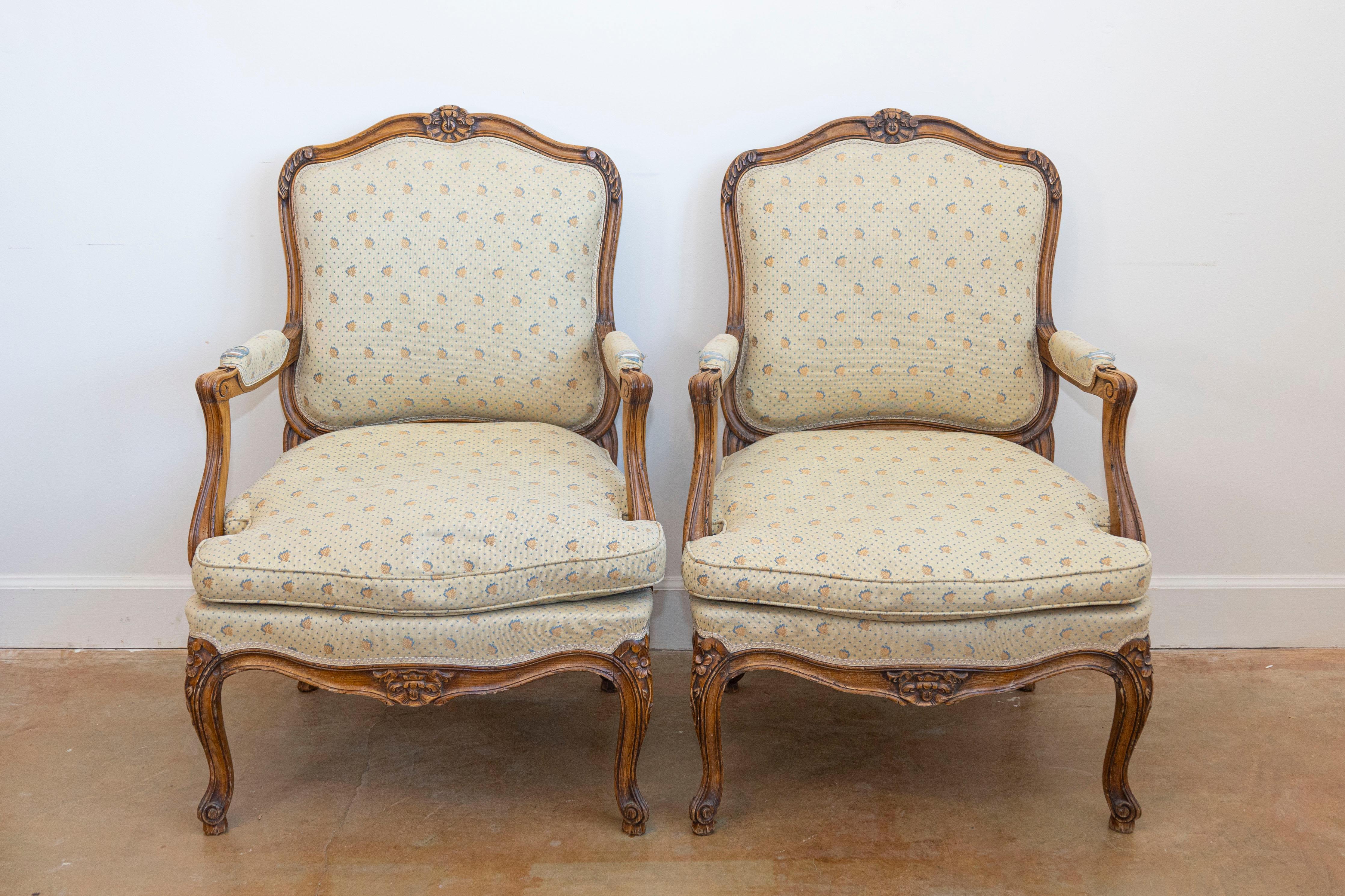 Coppia di poltrone francesi in stile Luigi XV in noce del XX secolo con decori floreali intagliati, nocche a voluta, gambe cabriole e imbottitura. Evocando la grandezza dei reali francesi, questa squisita coppia di poltrone in noce in stile Luigi