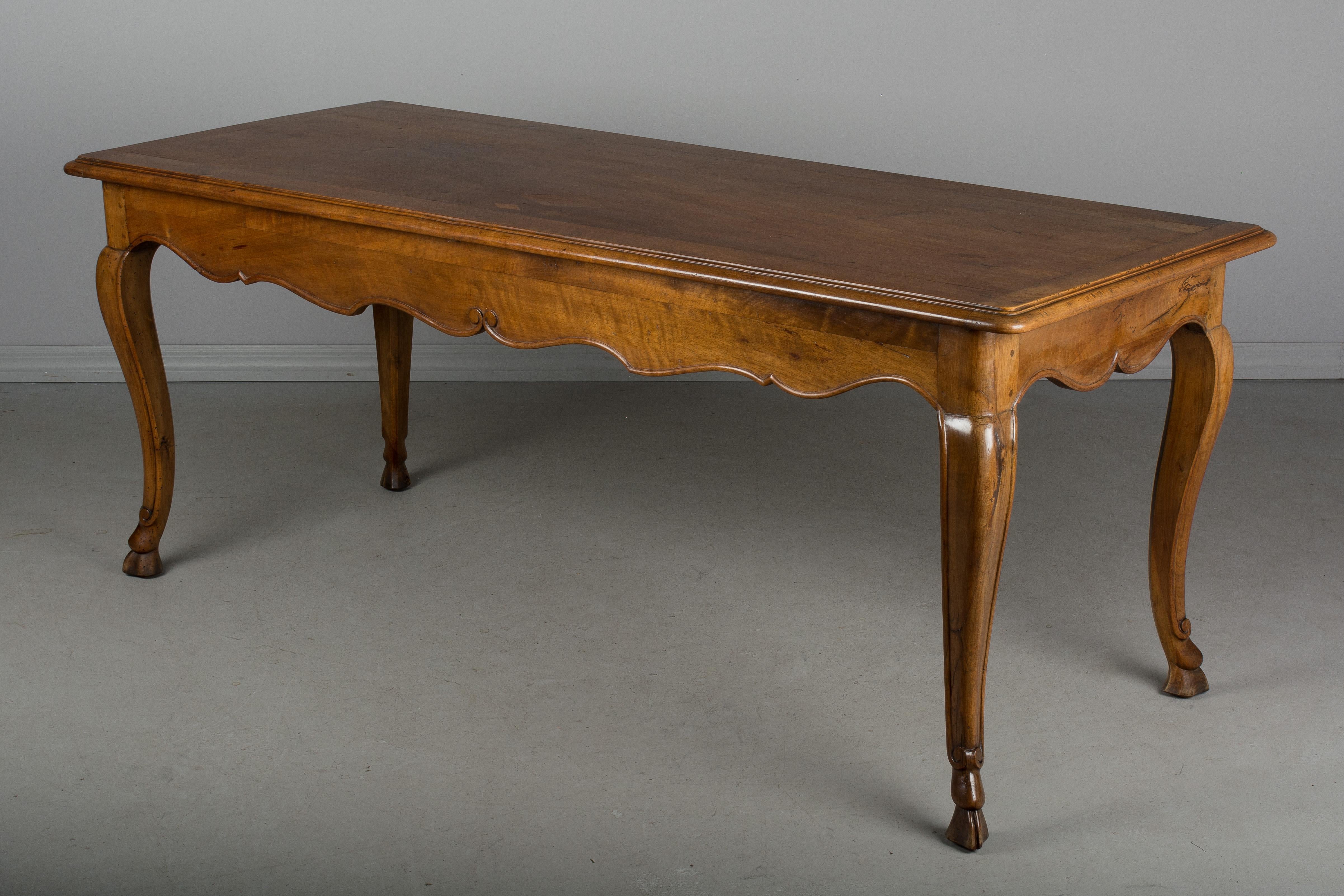 A beautiful Louis XV style Country French table made of solid walnut with decorative scalloped apron and cabriole legs ending in deer hoof feet. A sturdy table of good quality, crafted using pegged construction. Nice wood grain with waxed patina. A