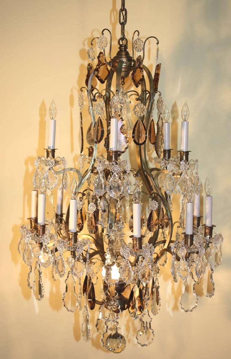 Lustre de style Louis XV en bronze doré et cristal avec quinze lumières sur deux niveaux, équipé de pendeloques françaises claires et ambrées, centrées par une fleur de clocher cannelée sur le baldaquin et une flèche creuse à la jointure inférieure,