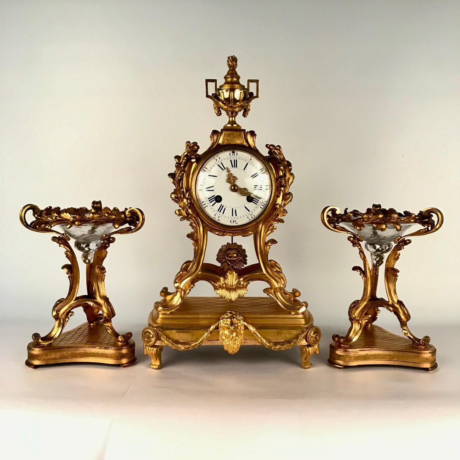 This fine garniture is of the spirit and period of the Belle Epoque It is certainly Belle, the barrel movement is supported by an extremely elegant acanthus and leaf-form frame, and surmounted by a classical vase with draping swag. The pendulum is