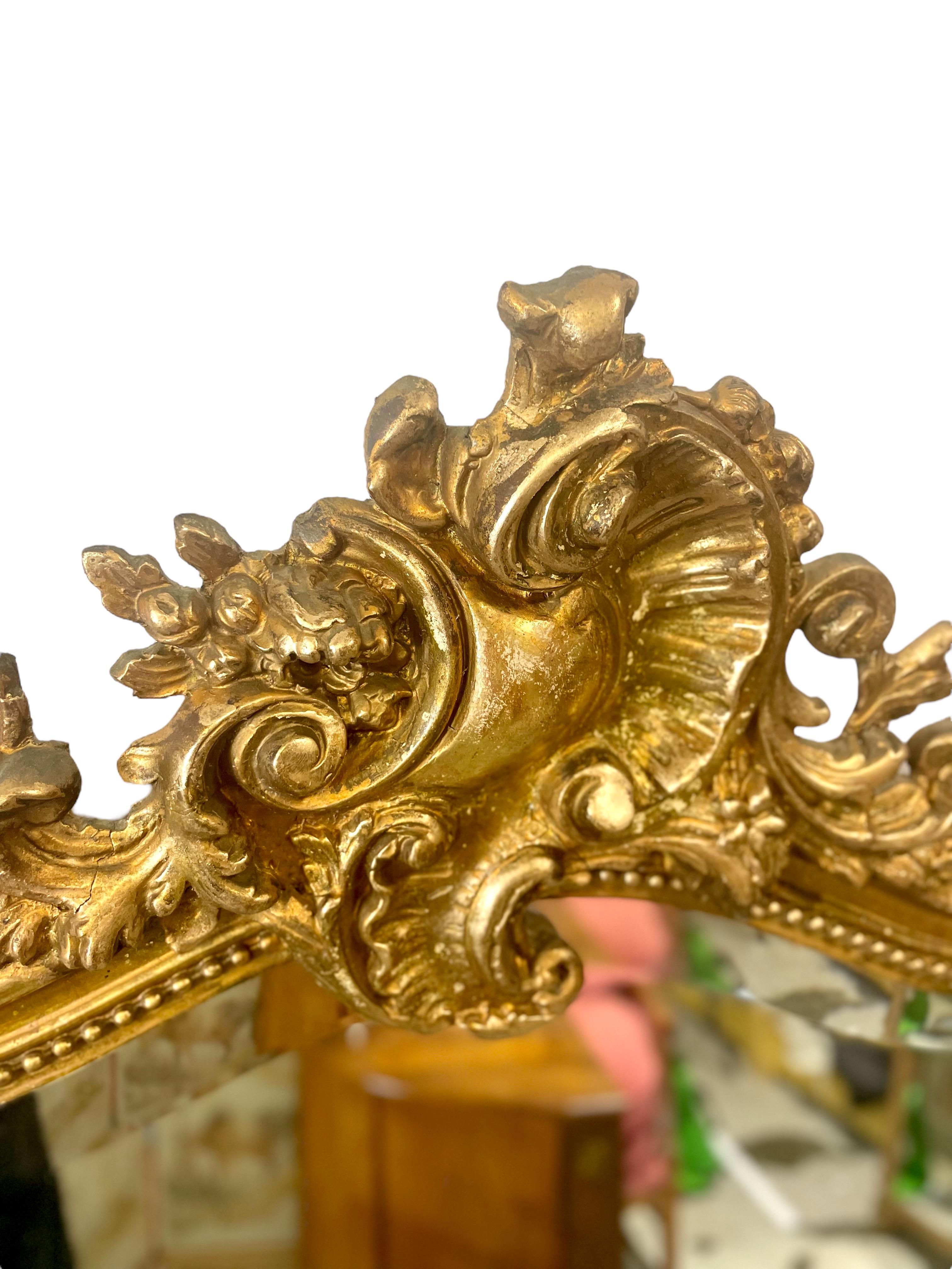A stunning 19th century Louis XV style overmantel mirror in wood and gilded stucco. An elaborately carved and out-sized asymmetric crest in a foliate scroll and stylised Rocaille motifs adorns the peak. The inner frame is decorated with a 'string of