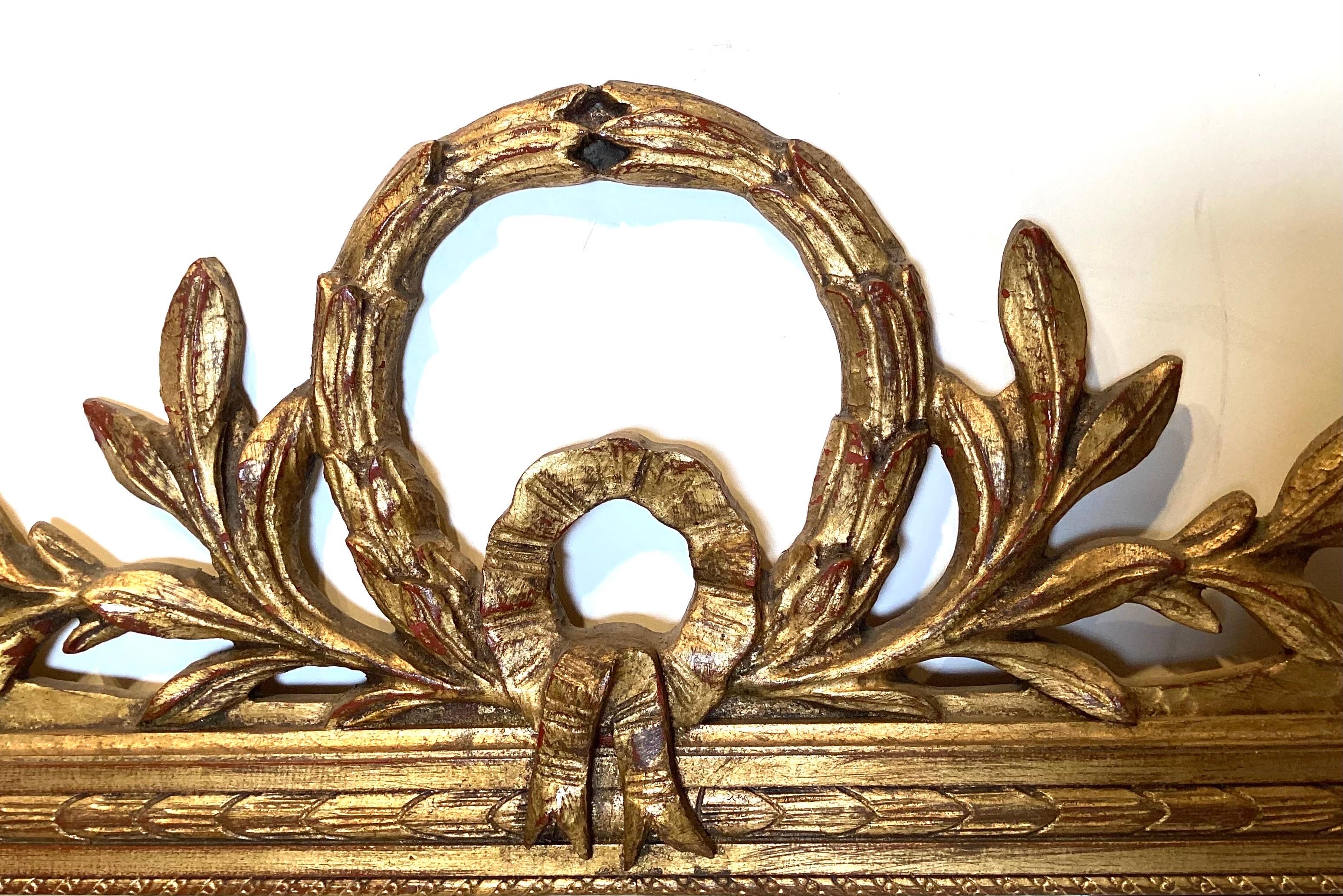 An Italian gilt wood mirror in the Louis XV style. The top pediment with wreath and olive branches with rosettes at the corners and reeded sides.