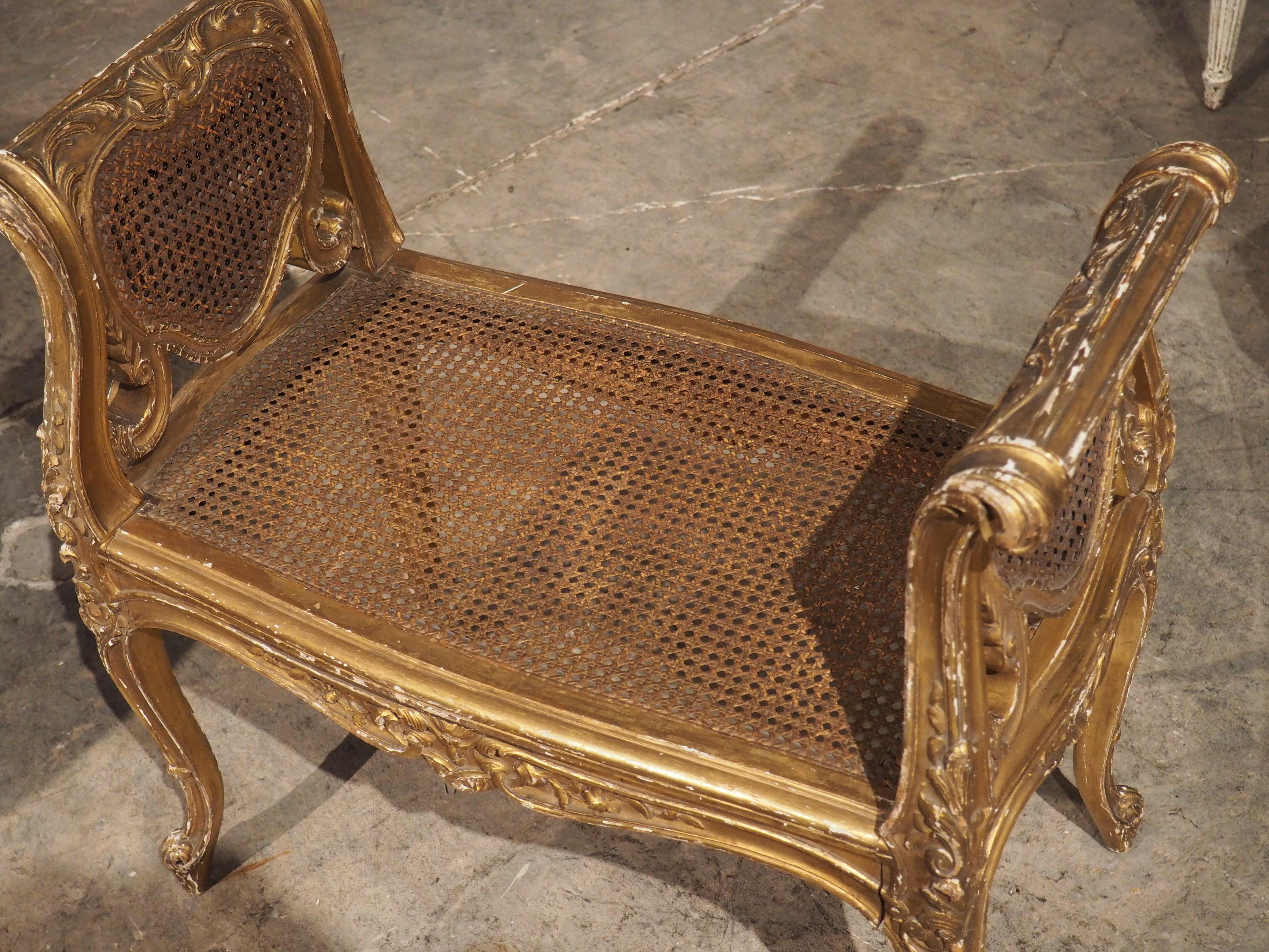 Hand-carved in France, circa 1850, this giltwood and caned banquette was produced in the style of Louis XV. Much like other seating from Louis XV, the banquette has carved arm supports and cabriole legs (four of them).

The seat is subtly shaped,