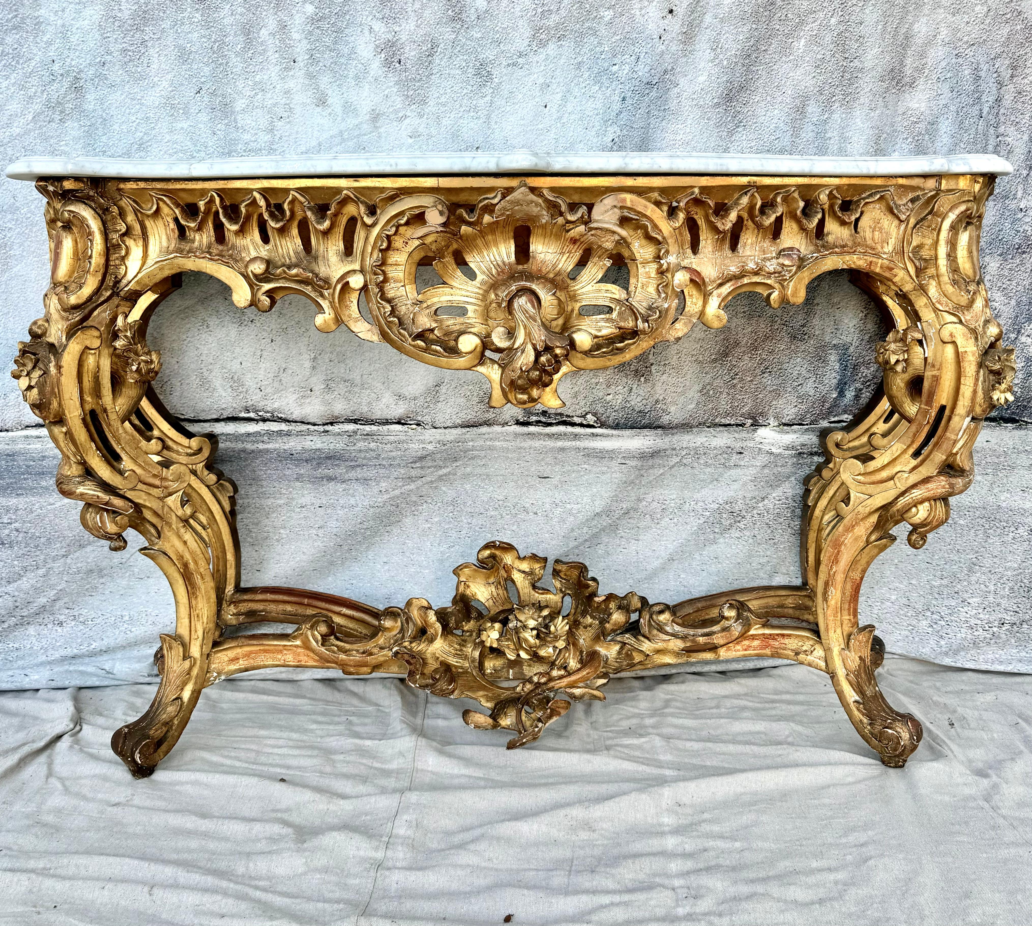 Early 19th Century Italian Louis XV Giltwood and Carrara Marble Top Console. This freestanding console table is raised by intricate carved cabriole legs on elegantly scrolled feet. Each leg is connected by an impressive giltwood foliate stretcher.