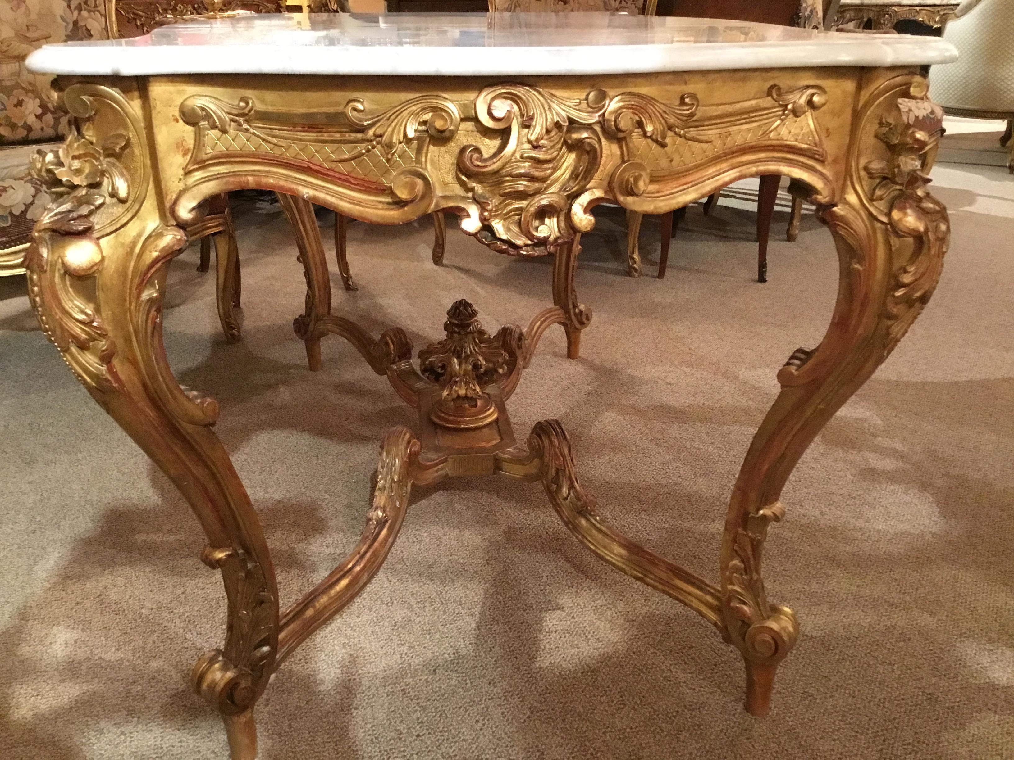 Mid-19th century giltwood center table, has a shaped rectangular white marble-top. The marble top is in pristine condition,
With a molded edge, above a conforming frieze centered by a central cartouche  design issuing foliate garlands to either