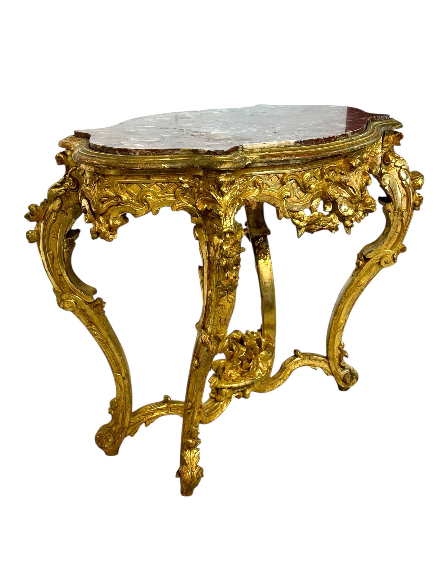 Magnífica mesa central de madera dorada estilo Luis XV del siglo XIX, con una elegante tapa de mármol Breccia serpentina en ricos tonos rojos y blancos. La base esculpida está finamente tallada a mano con hojas de acanto, guirnaldas florales y