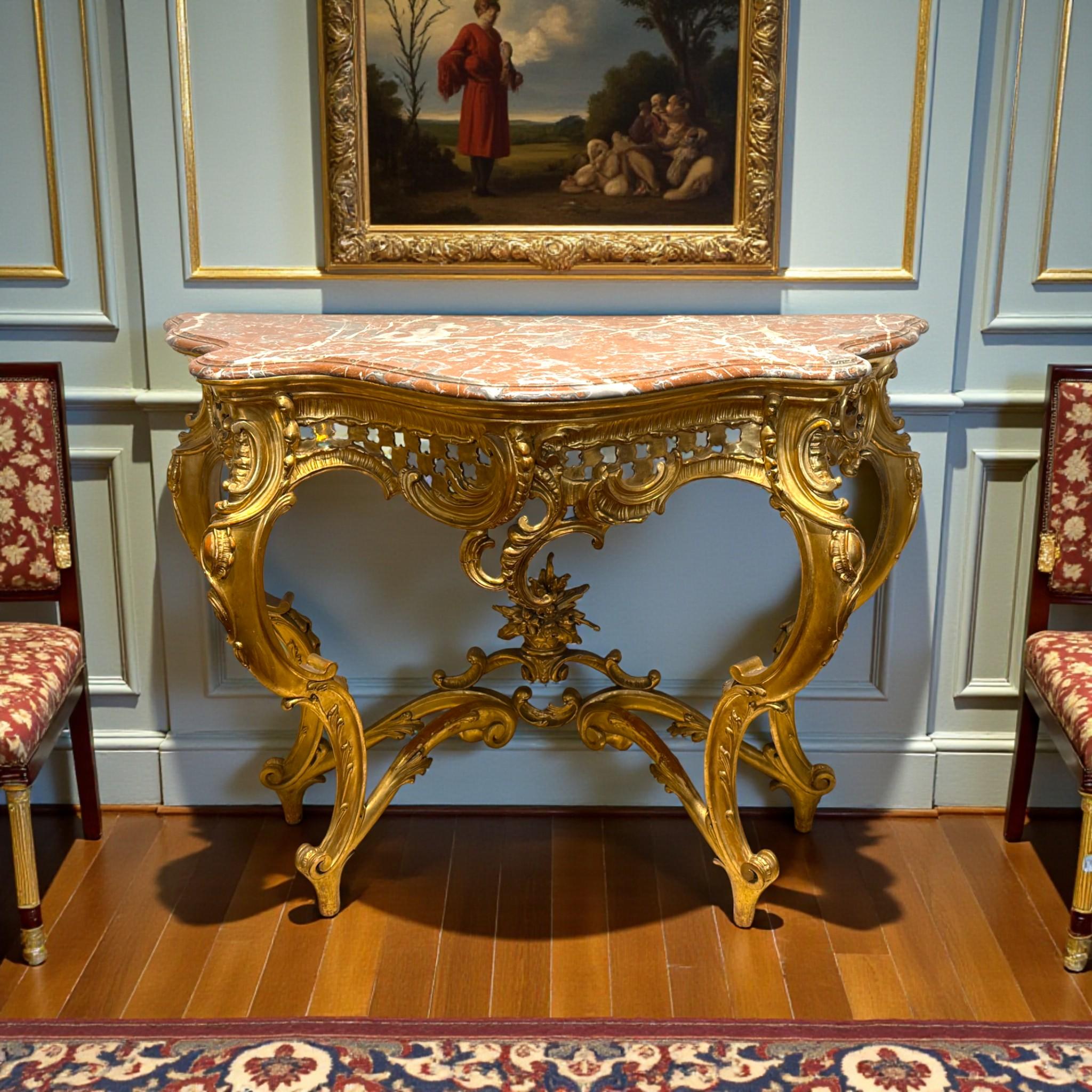 This refined Rococo-style console table embodies the elegance and artistic craftsmanship of the 19th-century French tradition. Fashioned in giltwood and supported by four graceful cabriole legs joined by an intricately carved stretcher, it displays