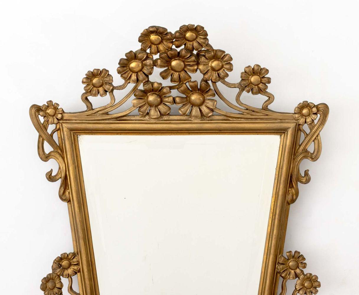 Espejo con marco de madera dorada y cristal biselado estilo Luis XV, de forma trapezoidal con cresta calada de motivos florales. Placa del espejo: 26,25