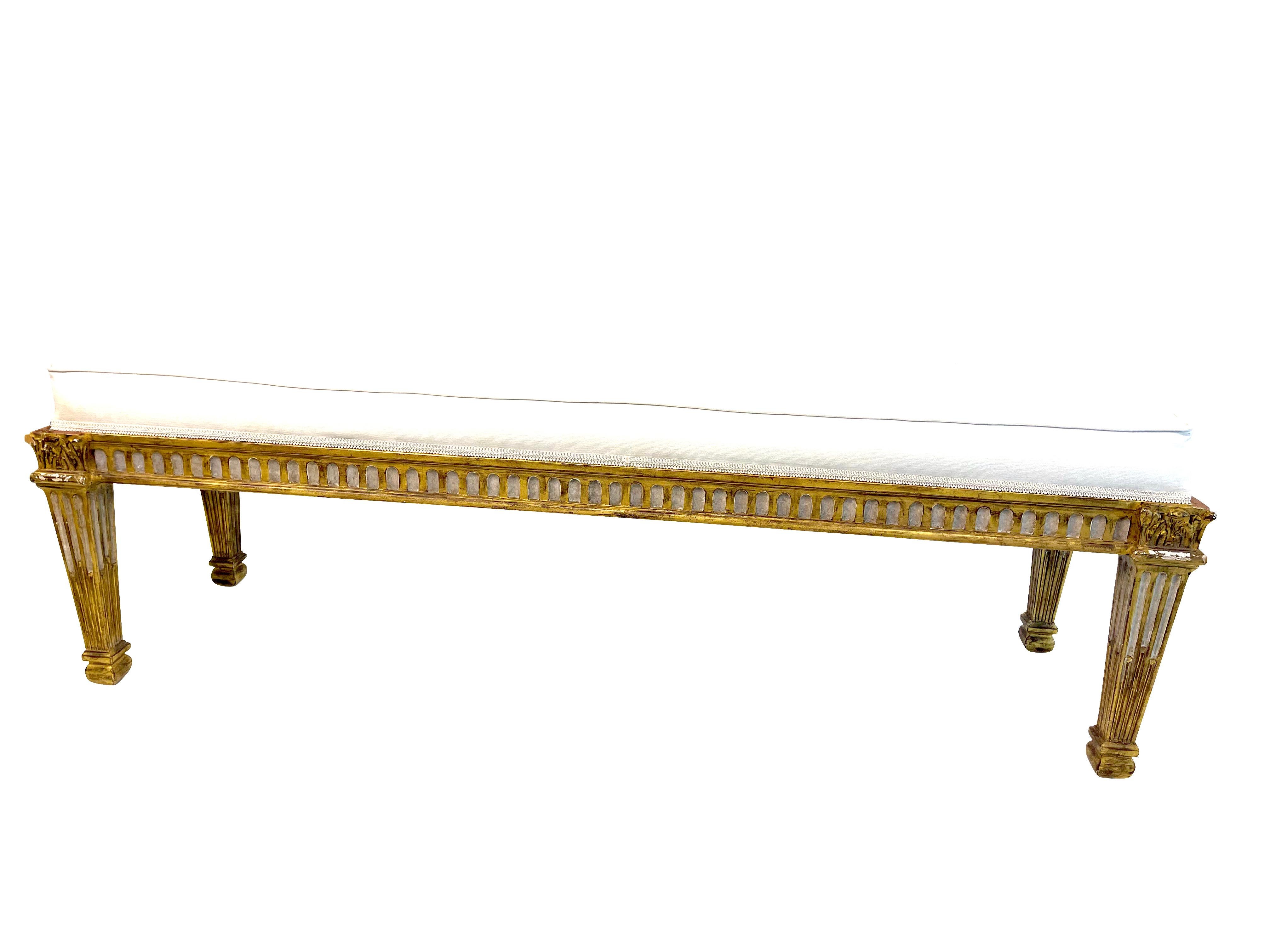 A decorative Louis XV-style gilt banquette or low bench perfect for the foot of your bed or in front of a fireplace. Highly decorative in gilt decoration with grey painted accents. Reeded legs and apron. This piece has been professionally