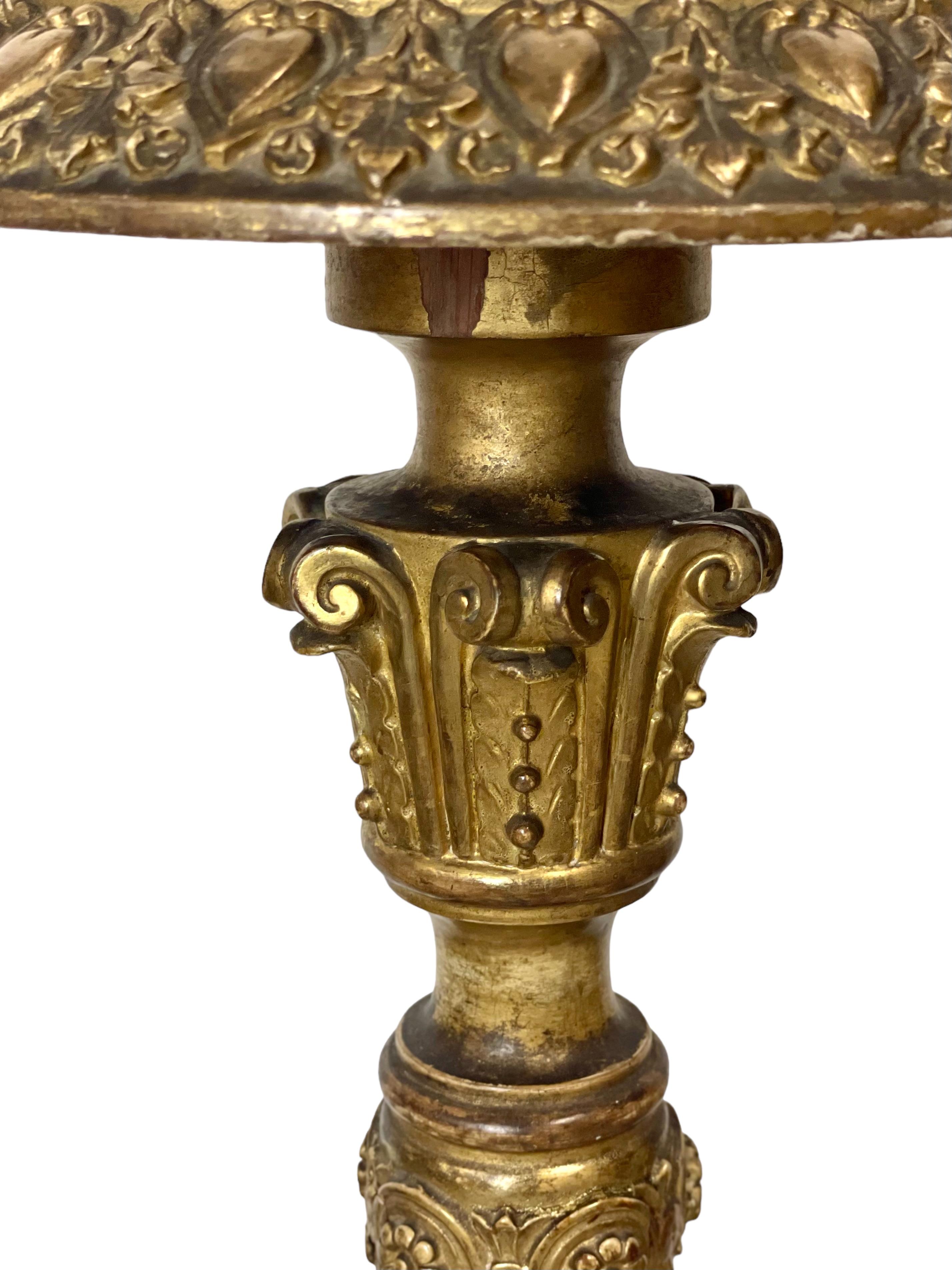 An antique French candle stand (or ‘torchère‘), in elaborately carved, gilded wood. This impressive Napoleon III period column pedestal support three features delicately carved feet encrusted with leaves and flowers, while the top is encircled by