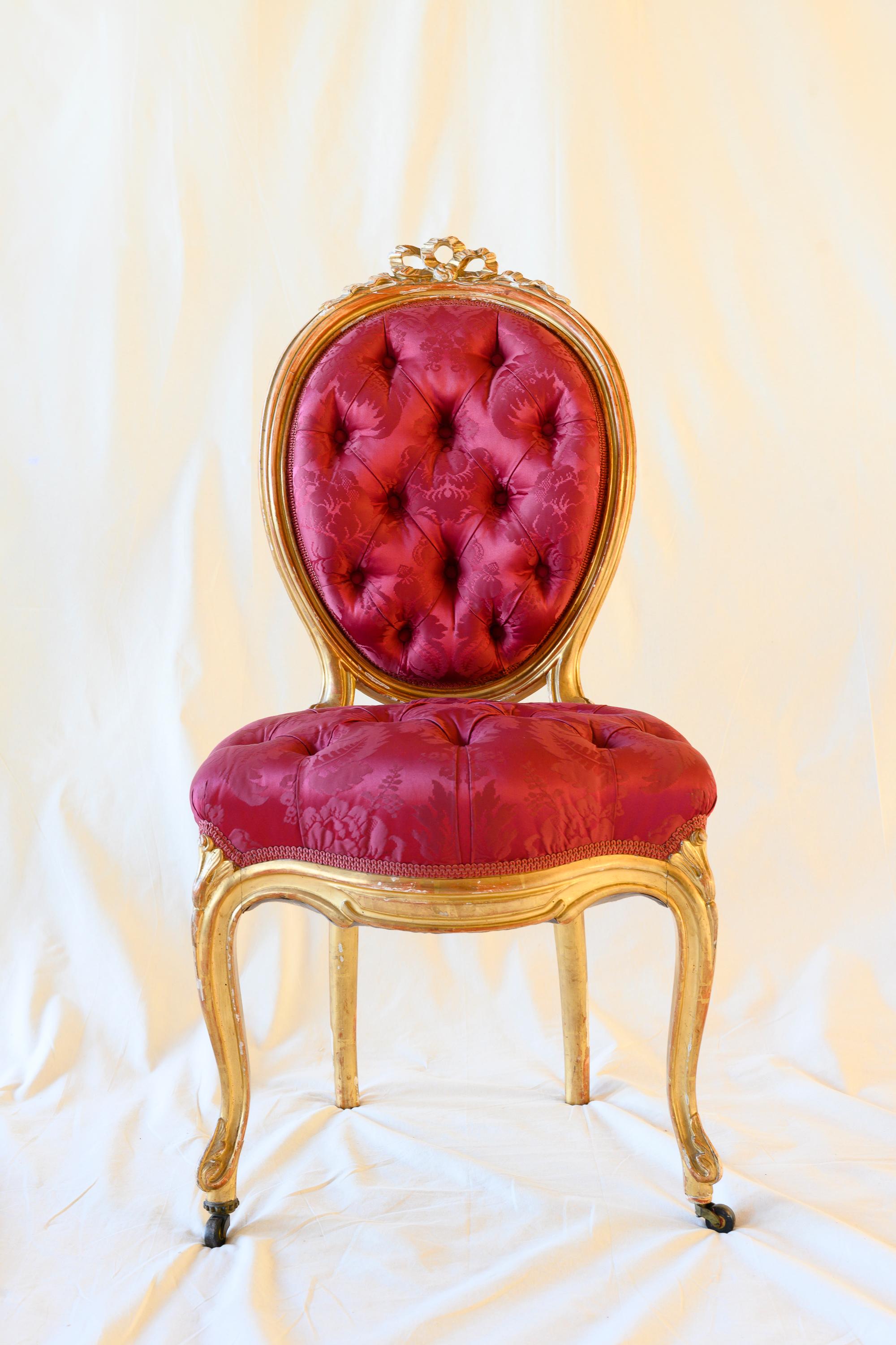 Suite of four Louis XV style giltwood cabriolet chairs. Comfortable curved round backrest carved with ribbons, supported on cabriole legs. Back and seat are deeply tufted in padded red silk, front feet are on castors. This suite of chairs remained