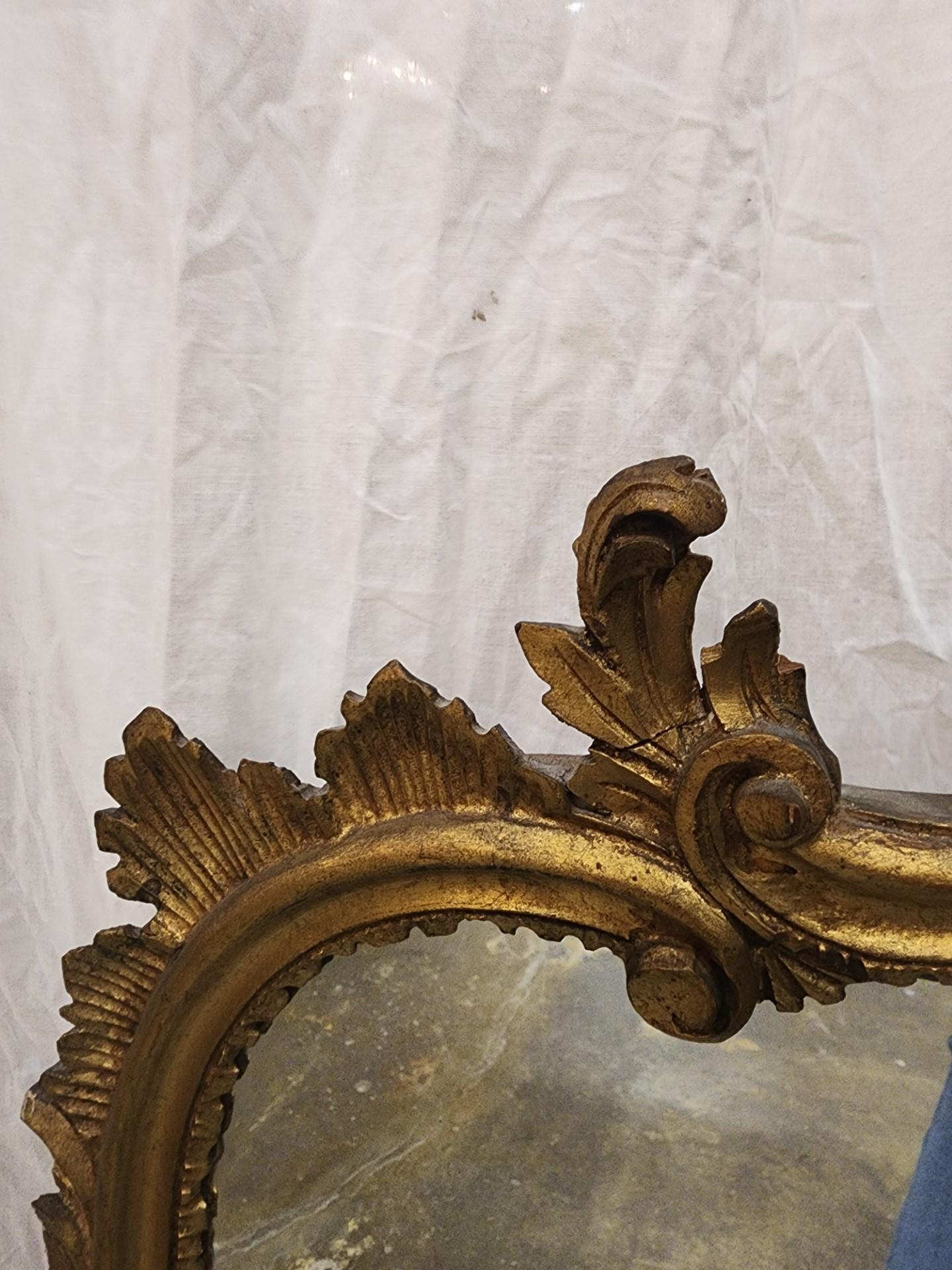 Miroir en bois doré de style Louis XV, fin C.C., avec une crête en éventail, sur un cadre en forme avec des motifs feuillagés, entourant une plaque de miroir plate.