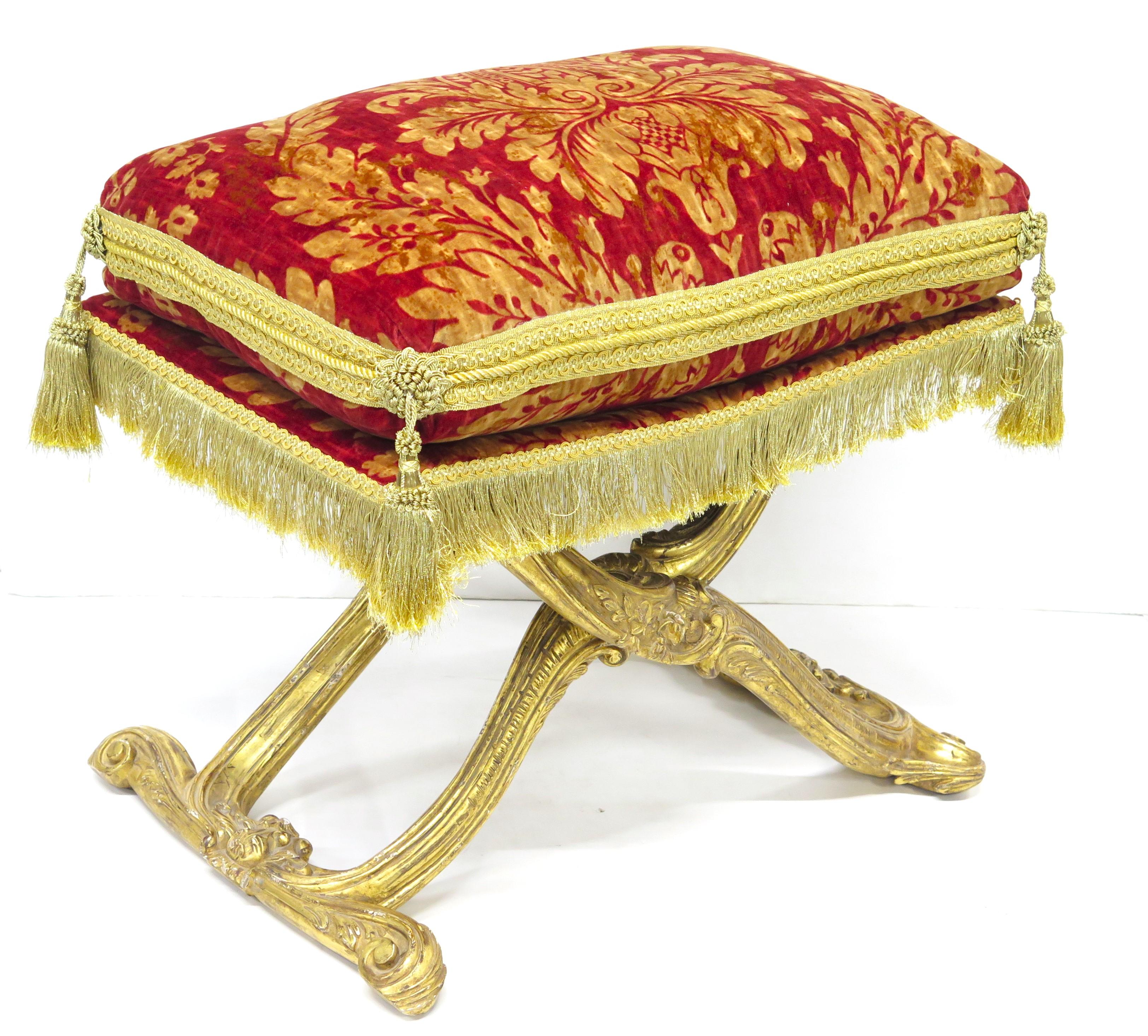 a Louis XV-style carved and gilded X-shaped folding stool / curule seat with a plump red and gold Damask printed velvet cushion / pillow with elaborate passementarie embellishments including gold braid, cord, trimmings, bullion fringe, and tassels,
