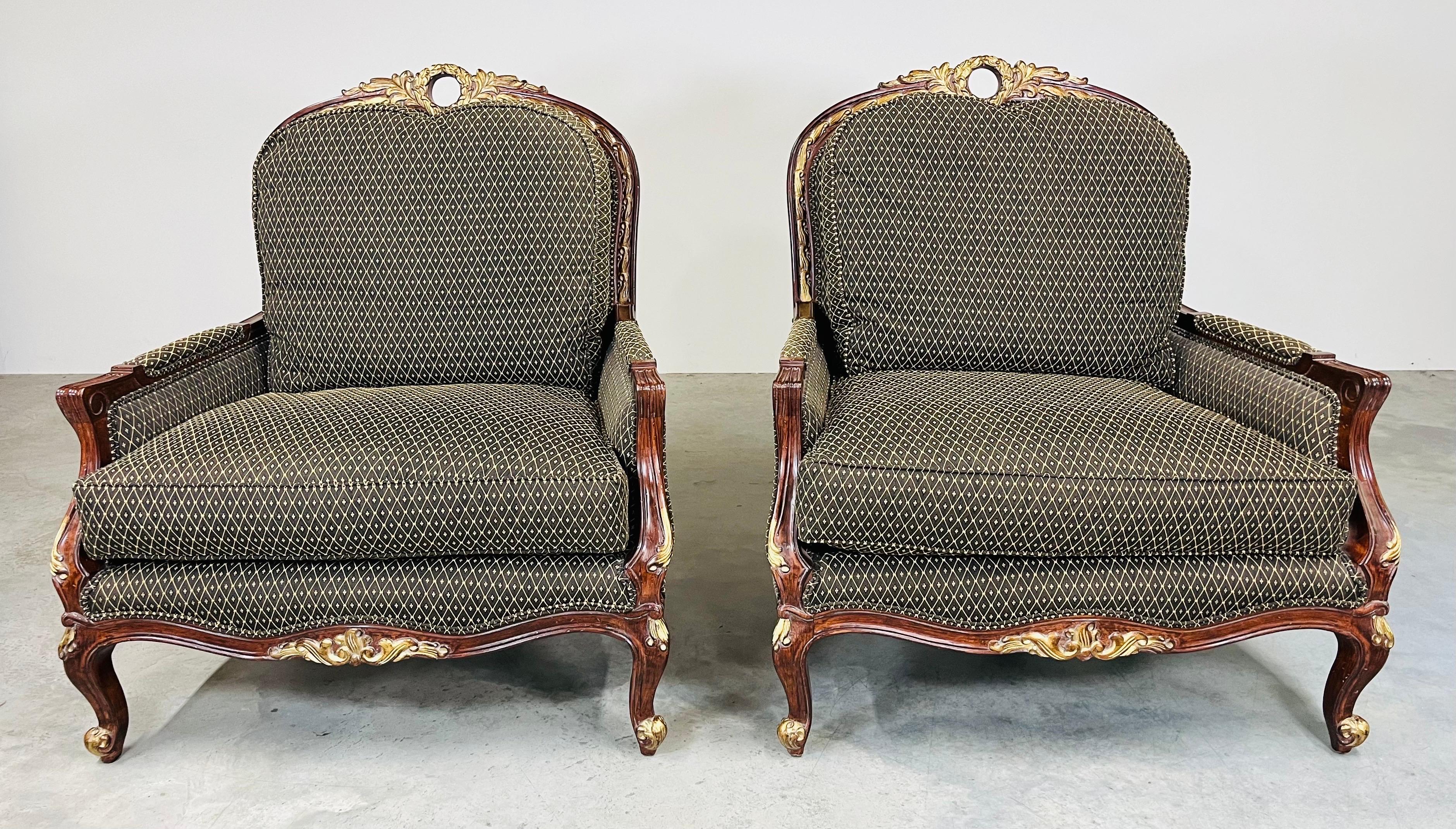 A beautiful pair of oversized Louis XV style bergere’ lounge chairs by Jeffco of North Carolina having mahogany frames with hand-carved gold gilt details throughout and overstuffed down cushions with gold toned upholstery that compliments the wood