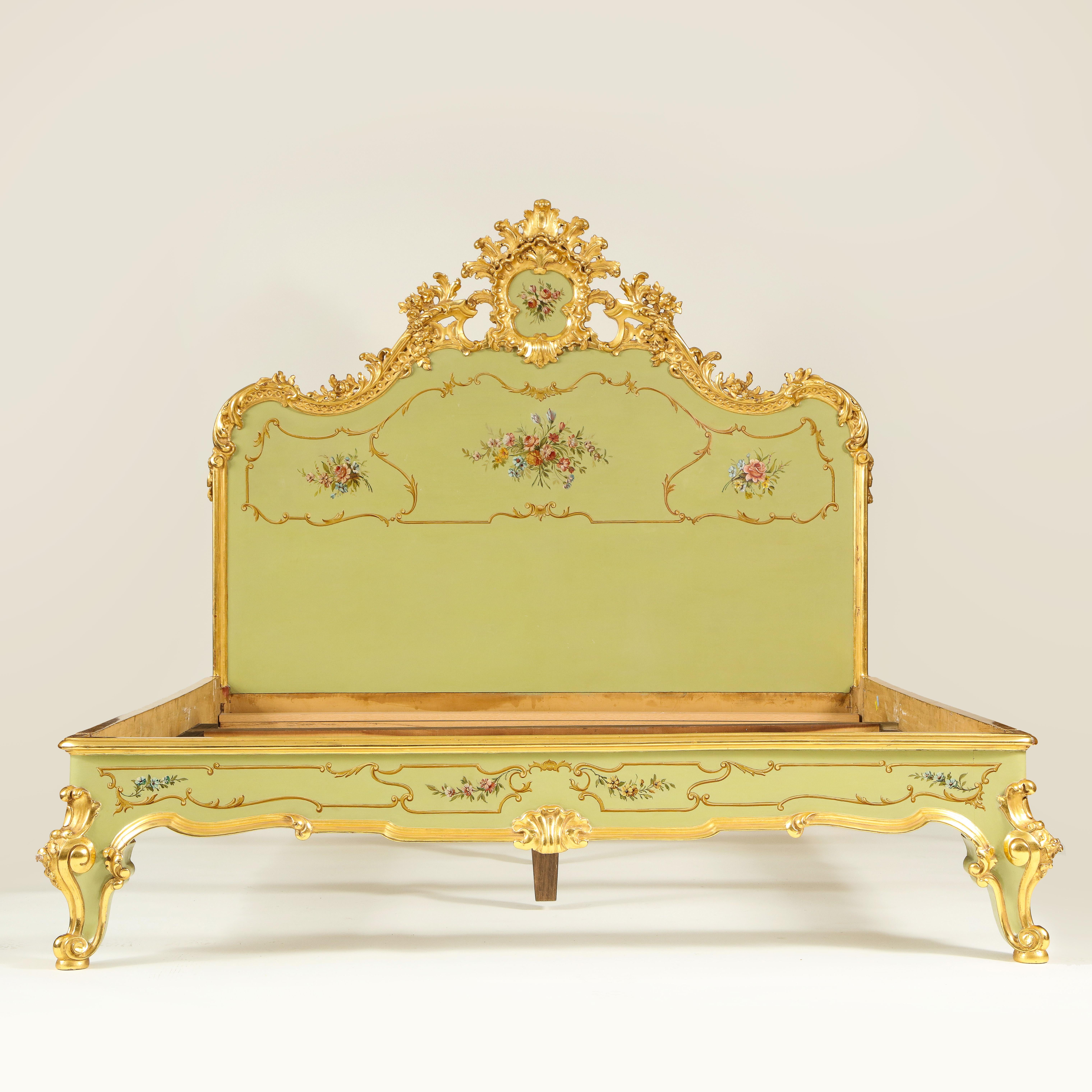 Comprising an arched headboard with parcel gilt cresting exuberantly carved with C-scrolls and centered by a cabochon-form cartouche hand painted with a floral bouquet; with a deep shaped frieze on out scrolled feet, decorated overall with floral