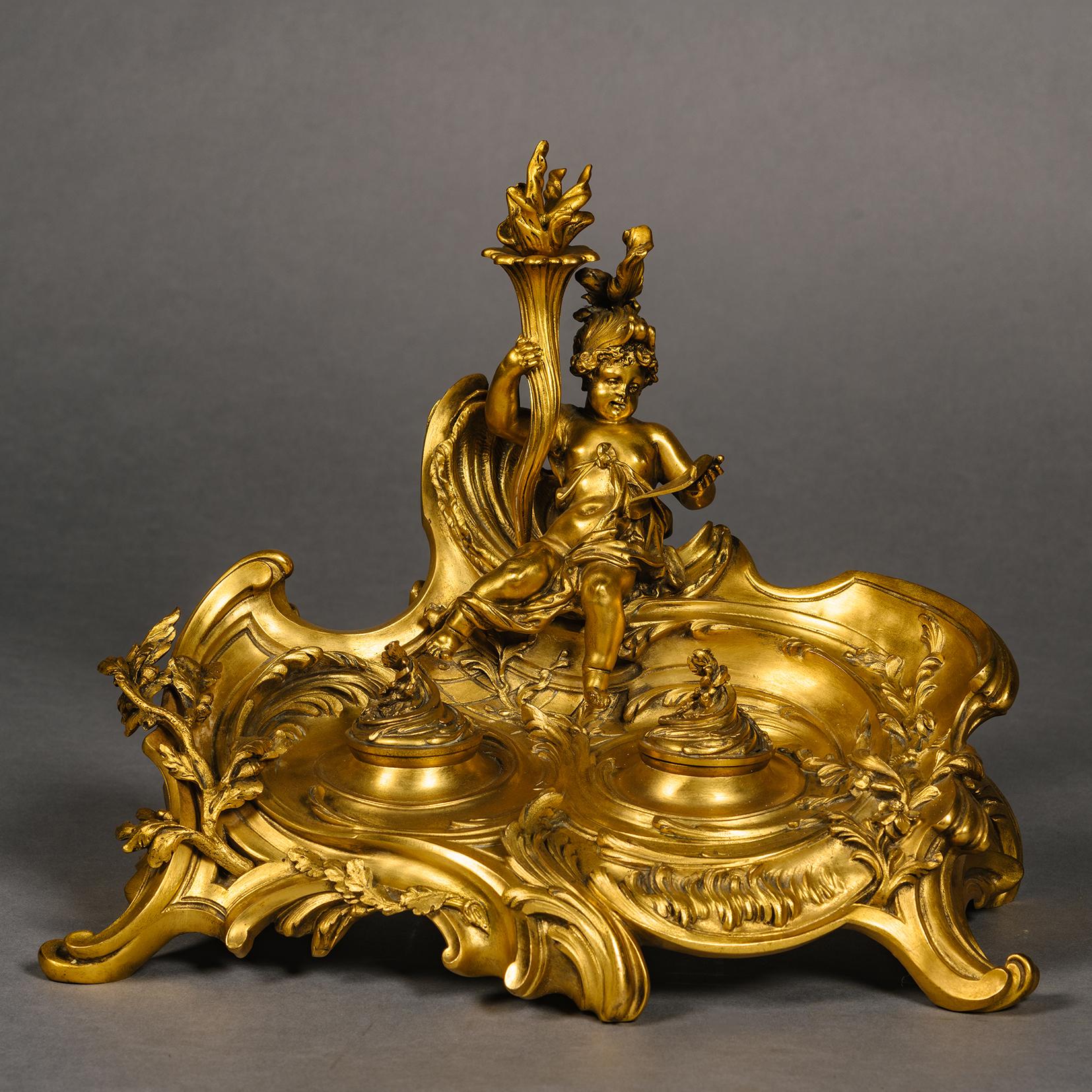 Seltenes vergoldetes Bronzetintenfass im Louis XV-Stil. Entworfen von Léon Messagé und gegossen von der Gießerei Ferdinand Barbedienne, Paris. 

Im überschwänglichen Rokokostil gestaltet, überragt von einer sitzenden Amor-Figur als Liebesbote, der