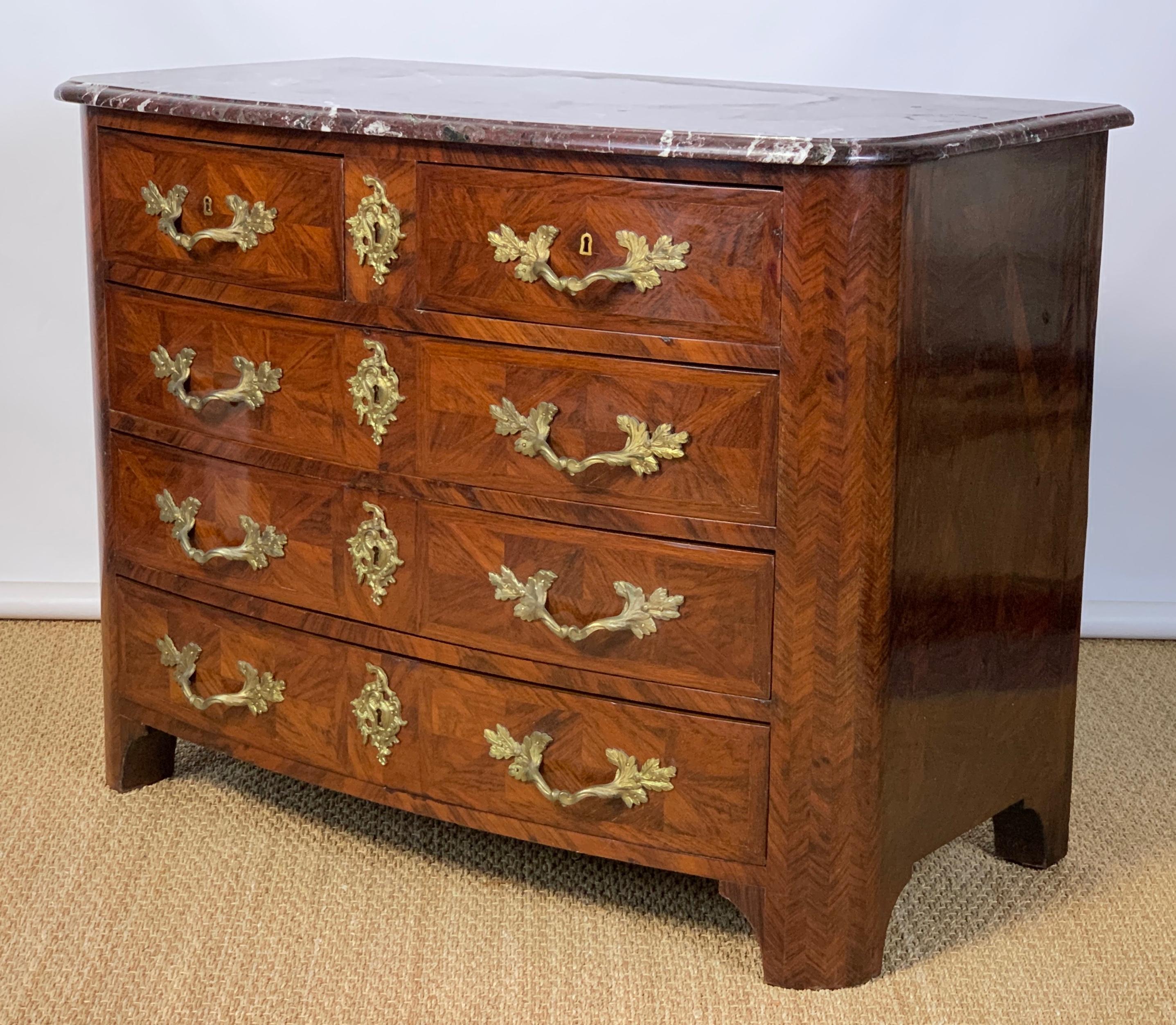 An elegant late 19th century French 5-drawer bow front commode in the Louis XV style featuring parquetry inlaid kingwood sides and front and elaborate gilt metal mounts with beautiful deep rose colored marble top.