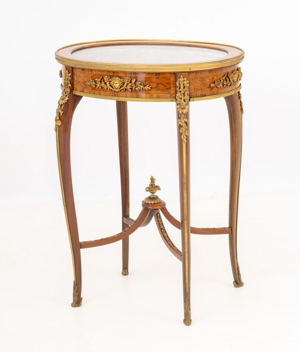 Mesa expositora ovalada de parquet de madera de rey estilo Luis XV, S. XIX, con monturas de ormolu sobre cuatro patas cabriolé unidas por cuatro camillas con ramo floral de bronce en el centro. 30