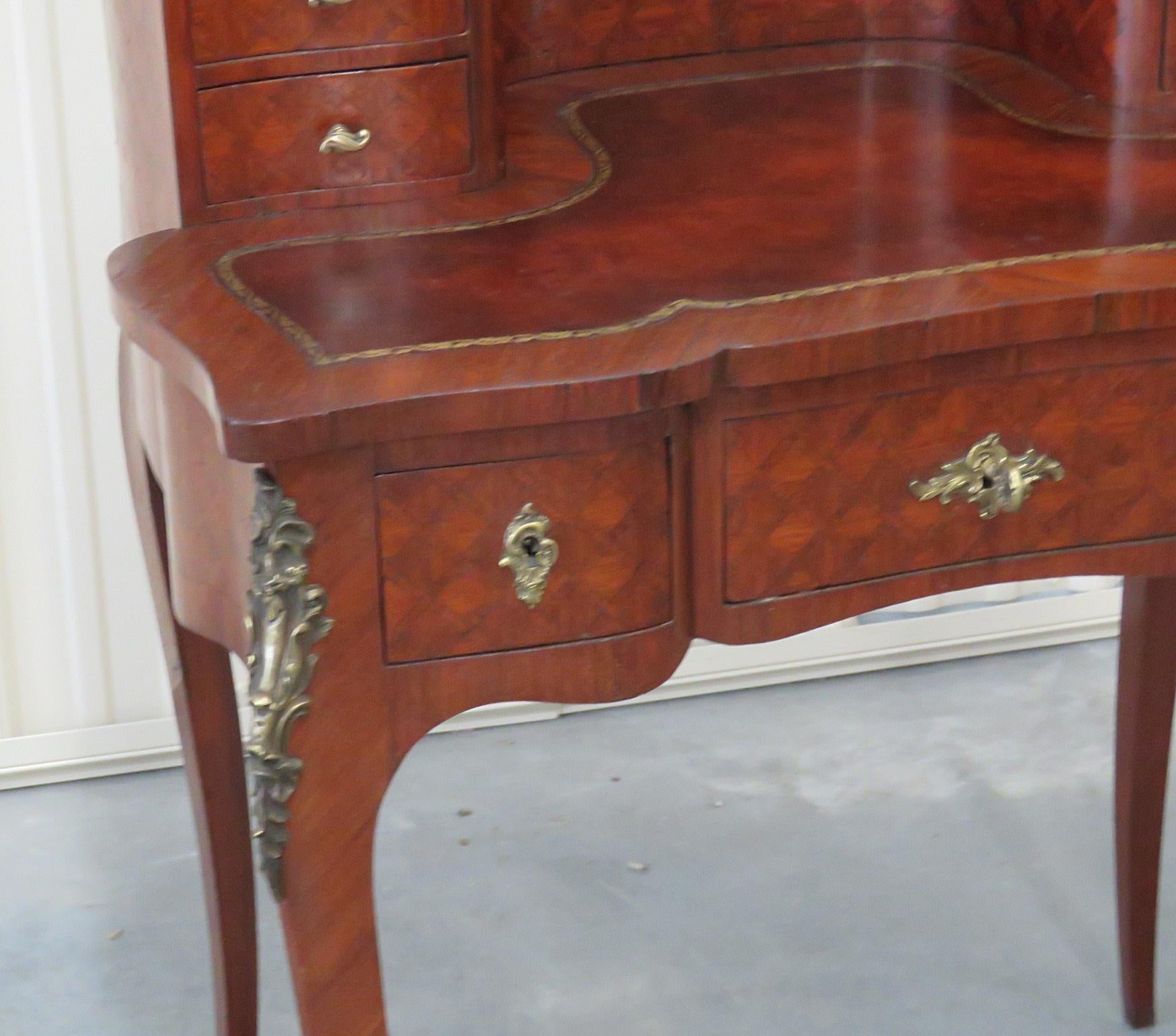 This is a very rare size of ladies desk. This Louis XV style inlaid 9-drawer ladies desk, in the manner of Maison Forest, has a leather top writing surface and a clock. The desk is adorned in beautifully cast bronze and in superb condition. The desk