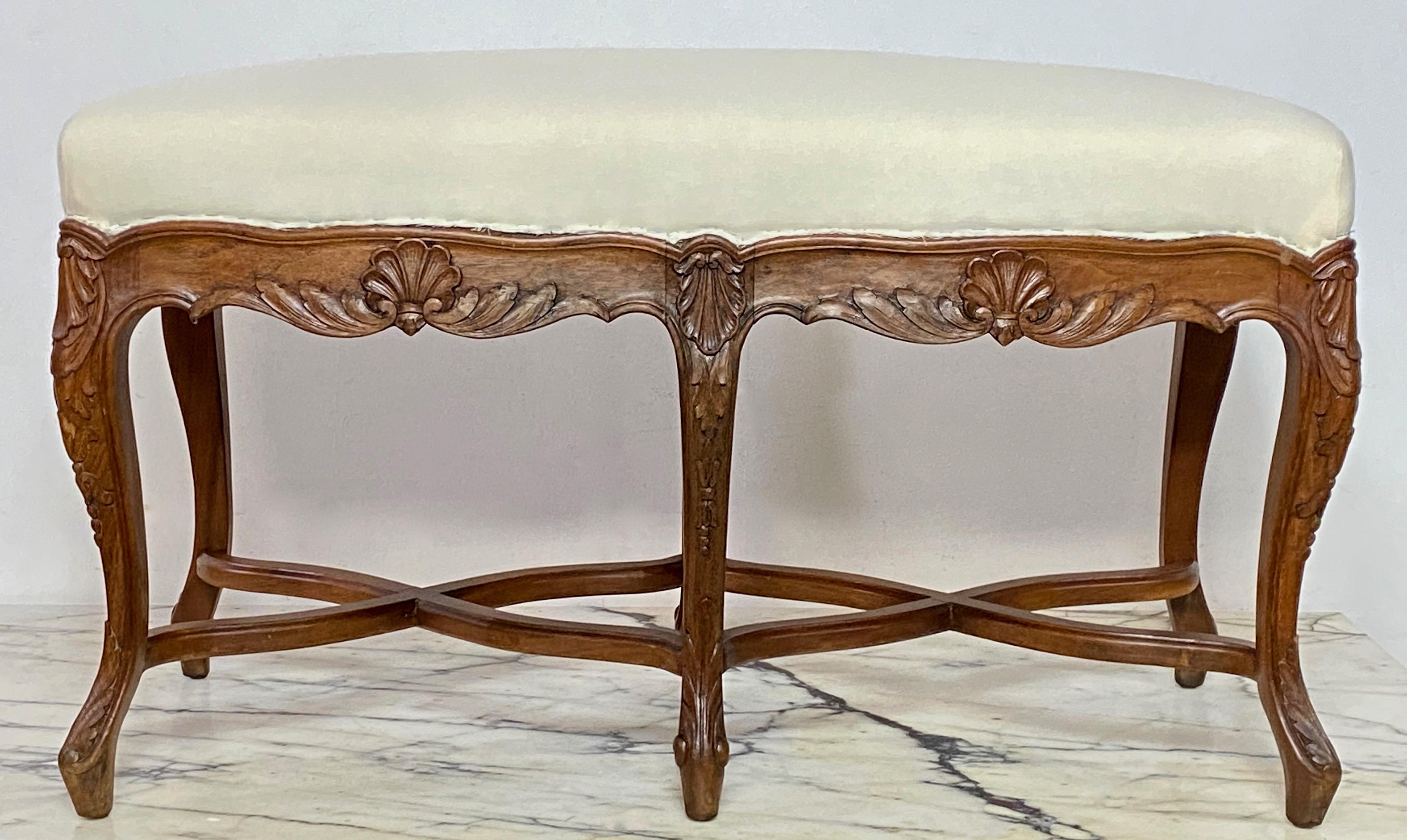 A Louis XV style long/ foyer upholstered bench in hand carved walnut,  with cabriole legs and double X-form stretchers.
Early 20th Century