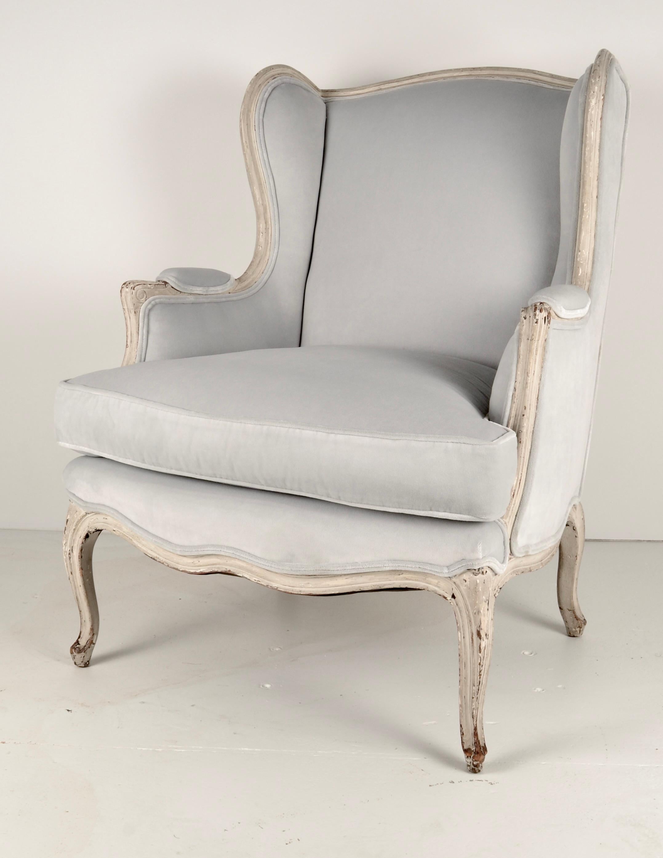 In the style of Louis XV, this French lounge chair with wing back details has wonderful patina on the fruitwood frame: natural wear of the original paint. The chair has been newly upholstered in a pale gray/blue quality velvet. Very fine condition.