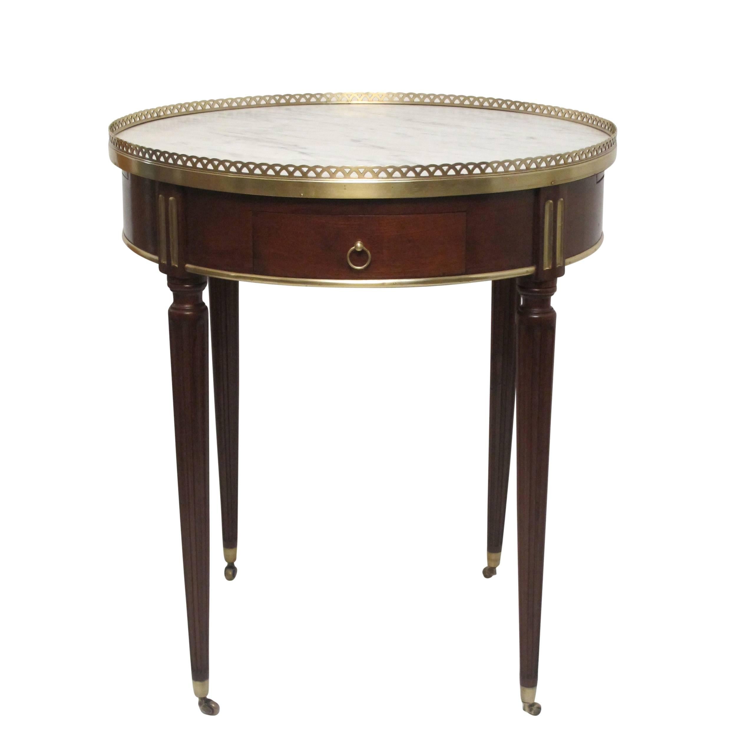 A Louis XV style mahogany bouillotte table, having a white marble top with gray veining, and a brass gallery. The table has two drawers and a pair of leather inlaid candle glides, France, mid-20th century, circa 1950.