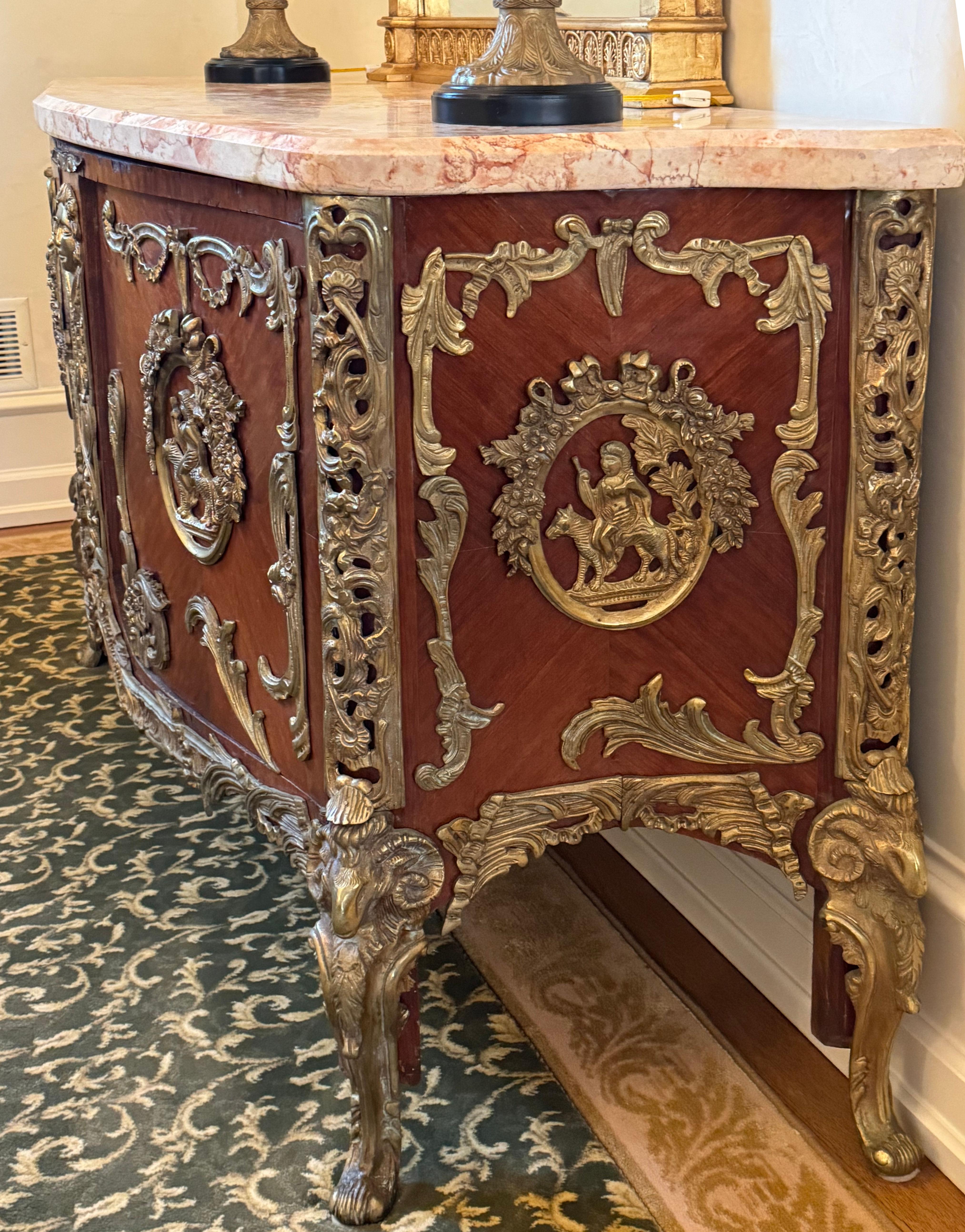 
Louis XV Style Marble Top Bronze Mounted Amaranth Commode
The veined molded serpentine marble top above a conforming case with two doors, each centering a bronze medallion of Bacchus atop a panther, the center post with a bronze female mask, the