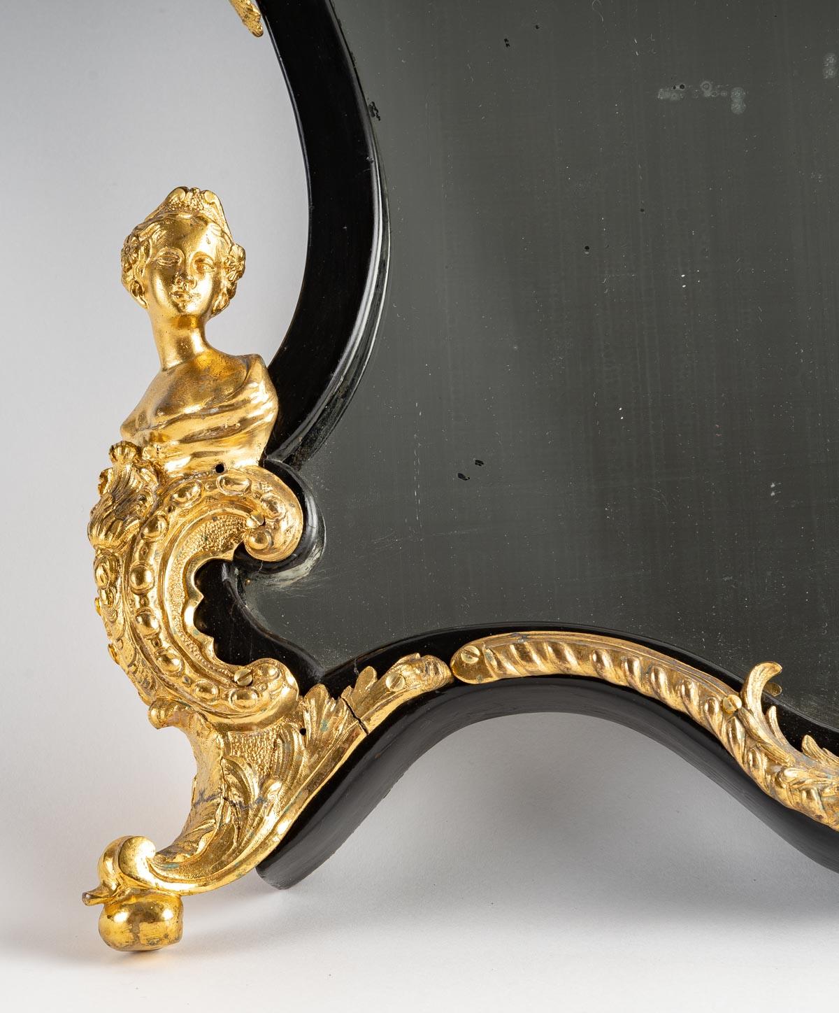 Miroir de style Louis XV, pouvant servir de miroir de table ou de miroir mural, en bronze doré, bois noirci. 1860-1880s
Dimensions : H : 57 cm, L : 44 cm, P : 9 cm.
 