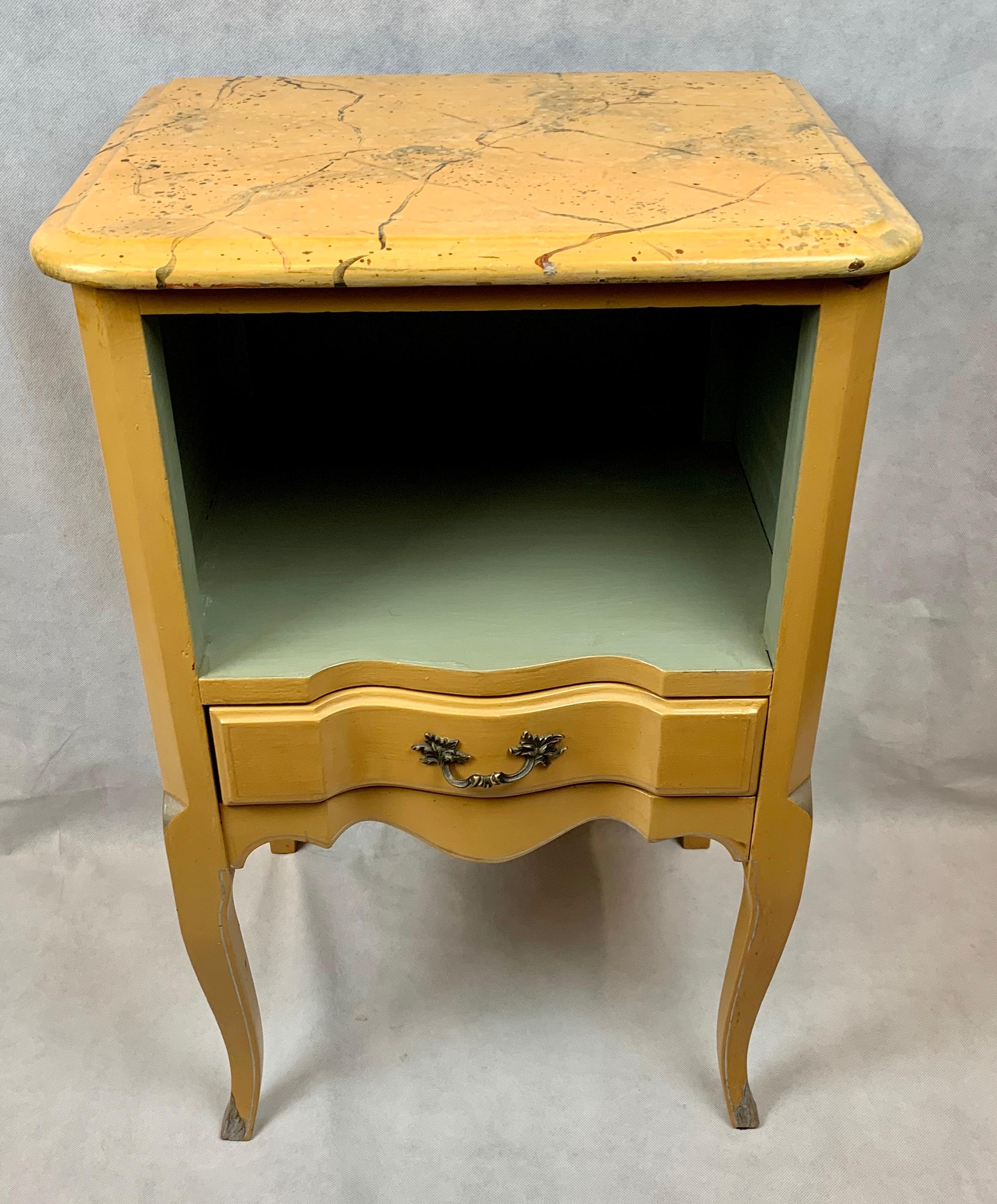 Louis XV style occasional or end table with a drawer.   This hardwood table in yellow paint has a faux marble top.  There is an open space for books or decorative objects. The drawer below has a brass pull. The legs are cabriole style, typical of