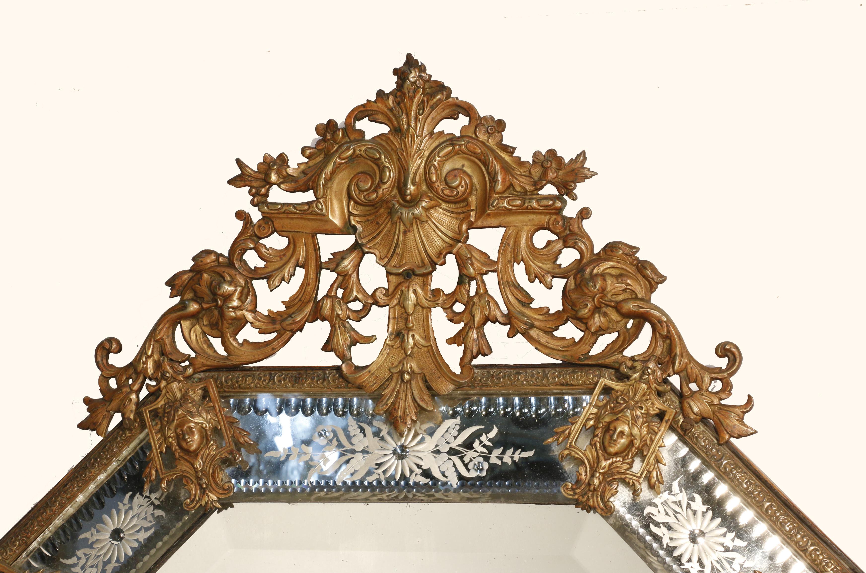 This mirror has a bevelled plate surrounded by verre eglomisee angled panels so there is much sparkle and reflection.
The elaborate pierced bronze crest is centred by a stylized shell with acanthus; a motif echoed at the base. 
A stylish touch is