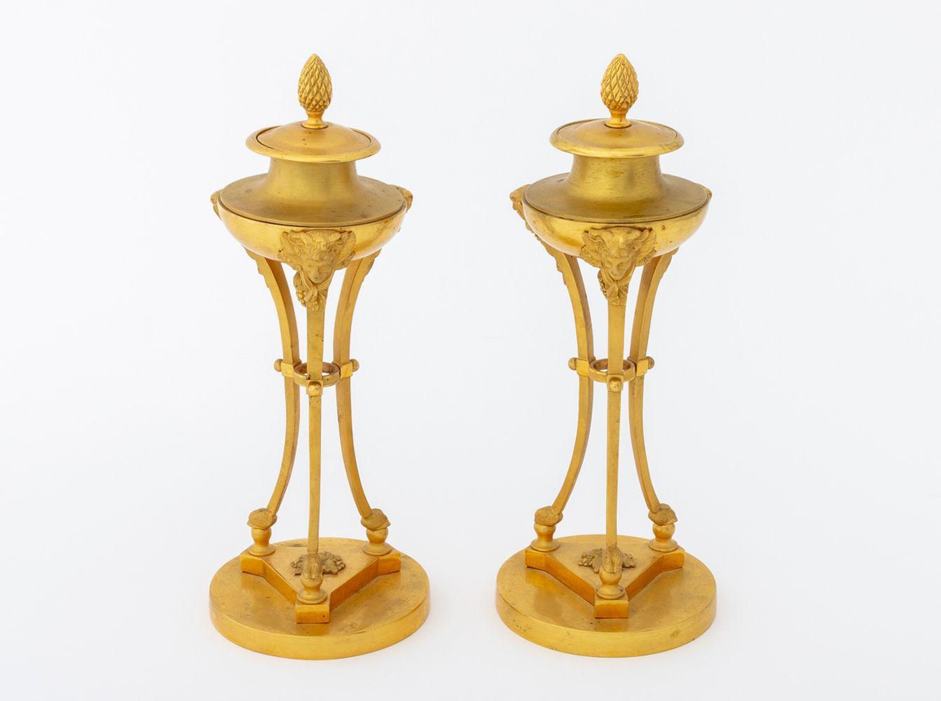 Pair of Louis XV Style Ormolu Cassolettes, late 19th century, the lids surmounted by pinecone finial, reversible and fitted with candlestick mount, on splayed tripod legs surmounted by masque heads, on hoof and ball feet, on circular base. 9.5