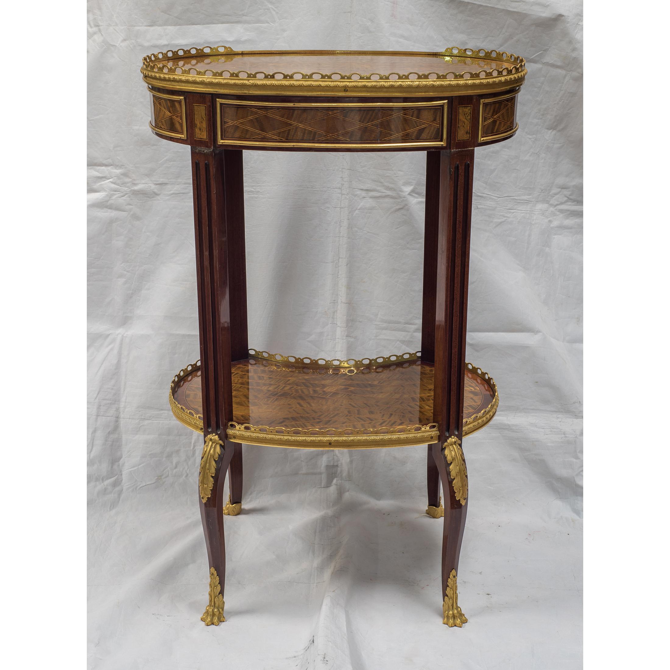 A stunning Louis XV-style ormolu-mounted inlaid tulipwood and mahogany galleried oval top table. The trelliswork inlaid three-quarter galleried oval top above a frieze drawer on fluted supports joined by a concave fronted platform stretcher, raised