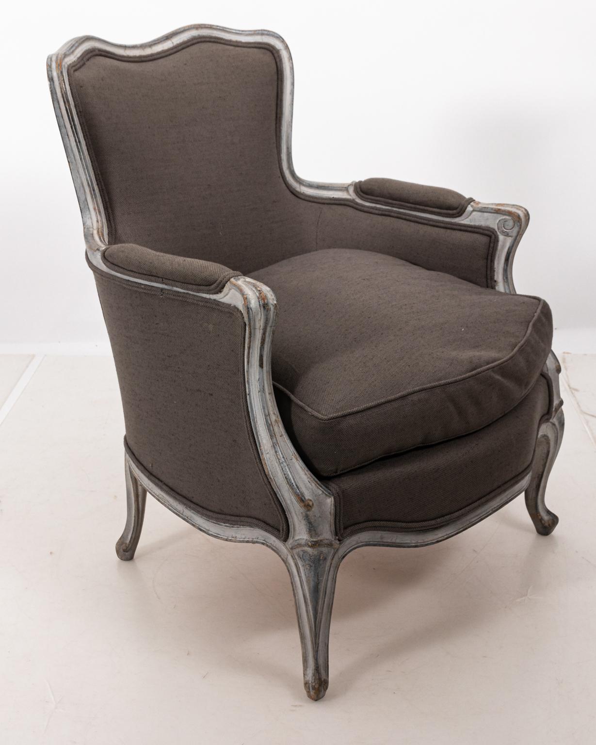 Louis XV style painted Bergère armchair with Rococo details such as cabriole legs. The piece is also upholstered in grey Belgian linen. Please note of wear consistent with age including distressed finish to the wood frame and minor paint loss.