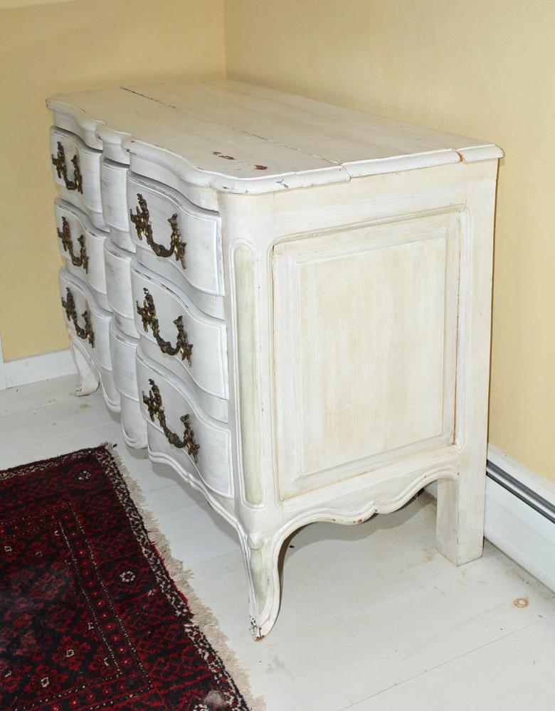The Louis XV-style dresser is painted white and has three drawers with large elaborate metal handles The sides are paneled in the French manner.