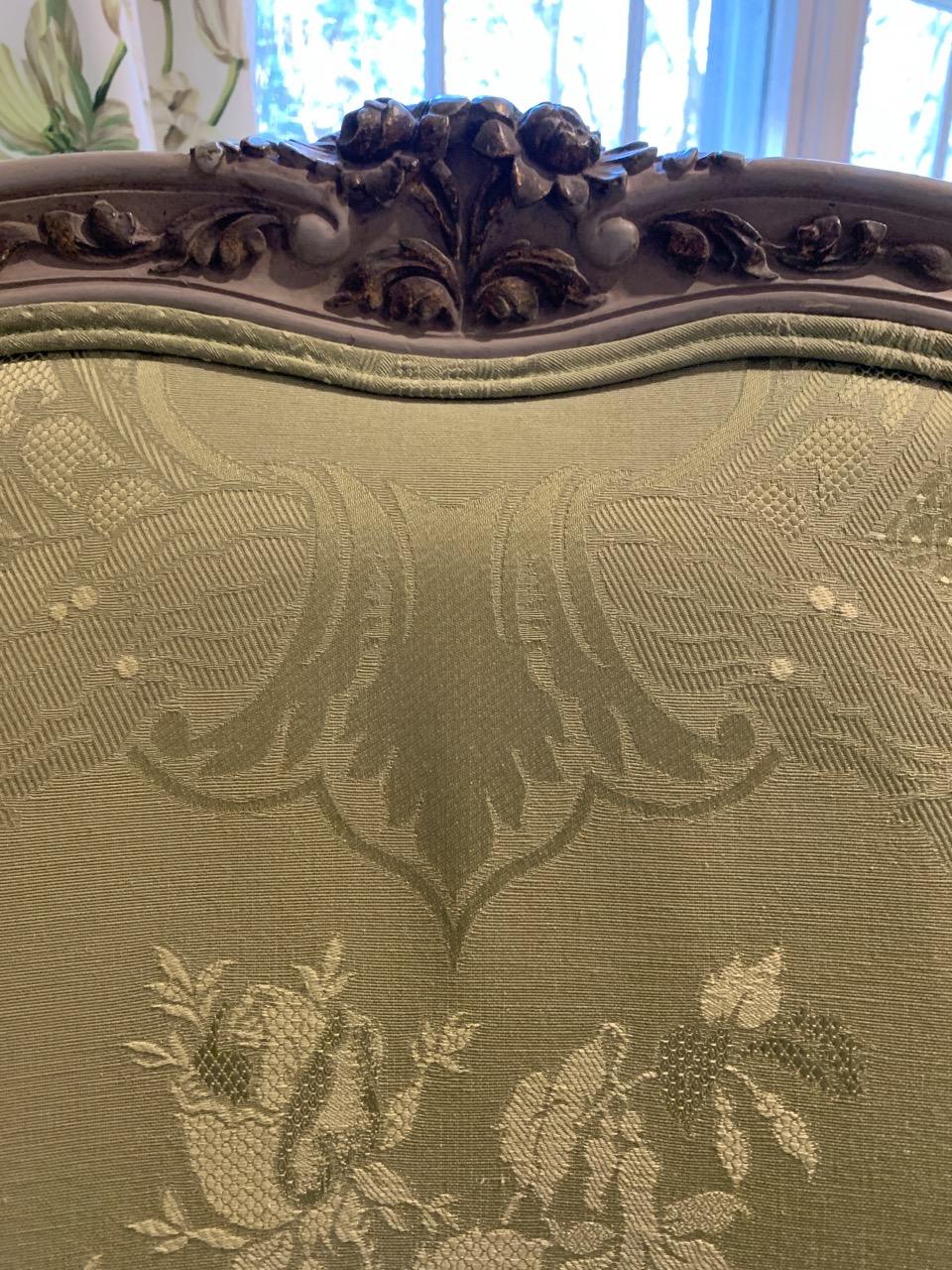 Louis XV style carved cream painted and gilt beechwood frame pale green damask upholstered bergère, having an arched cresting of carved gilt flowers and exuberant wings, padded arms and fluted arm supports , loose seat cushion and throw pillow,