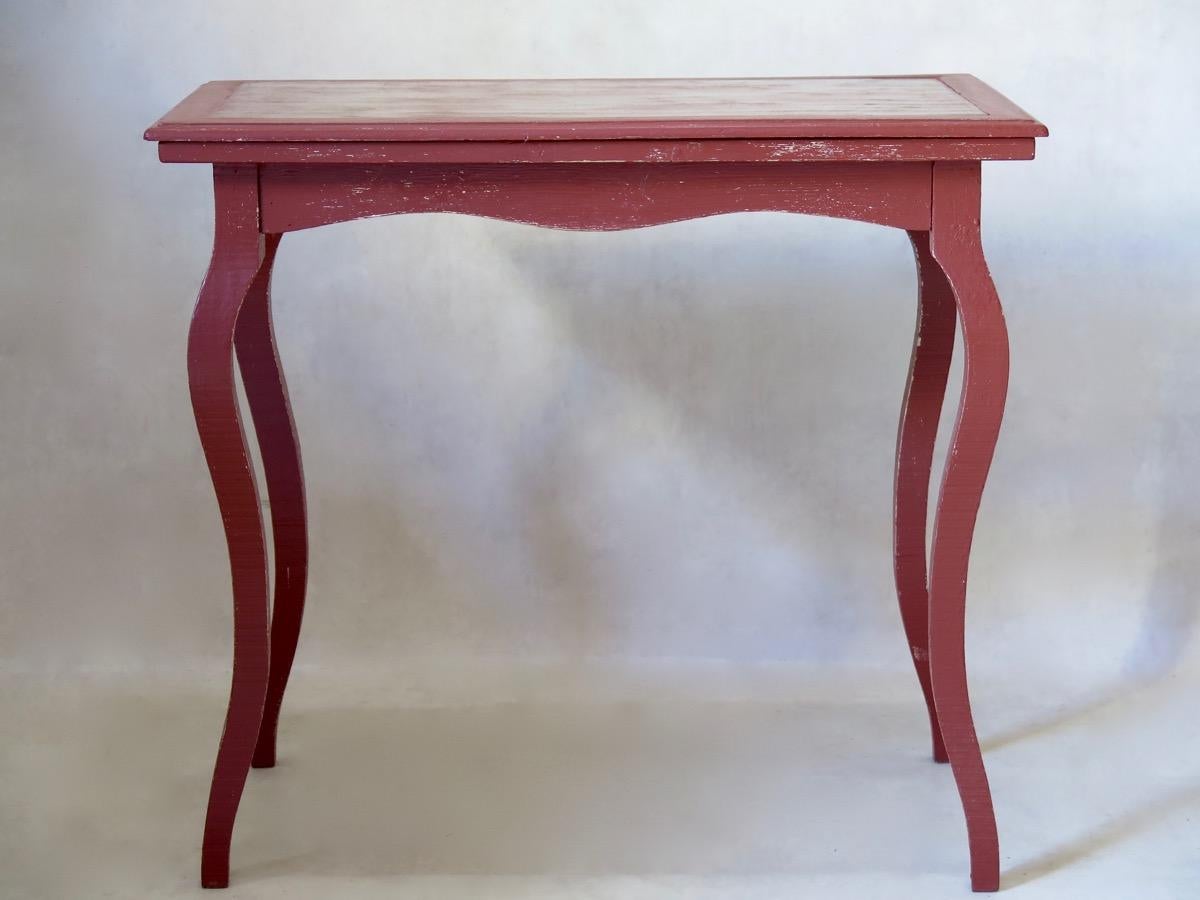 Small rectangular wooden table, painted oxblood red. The top has a thick, frosted glass pane, and is raised on elegant, cabriole legs.