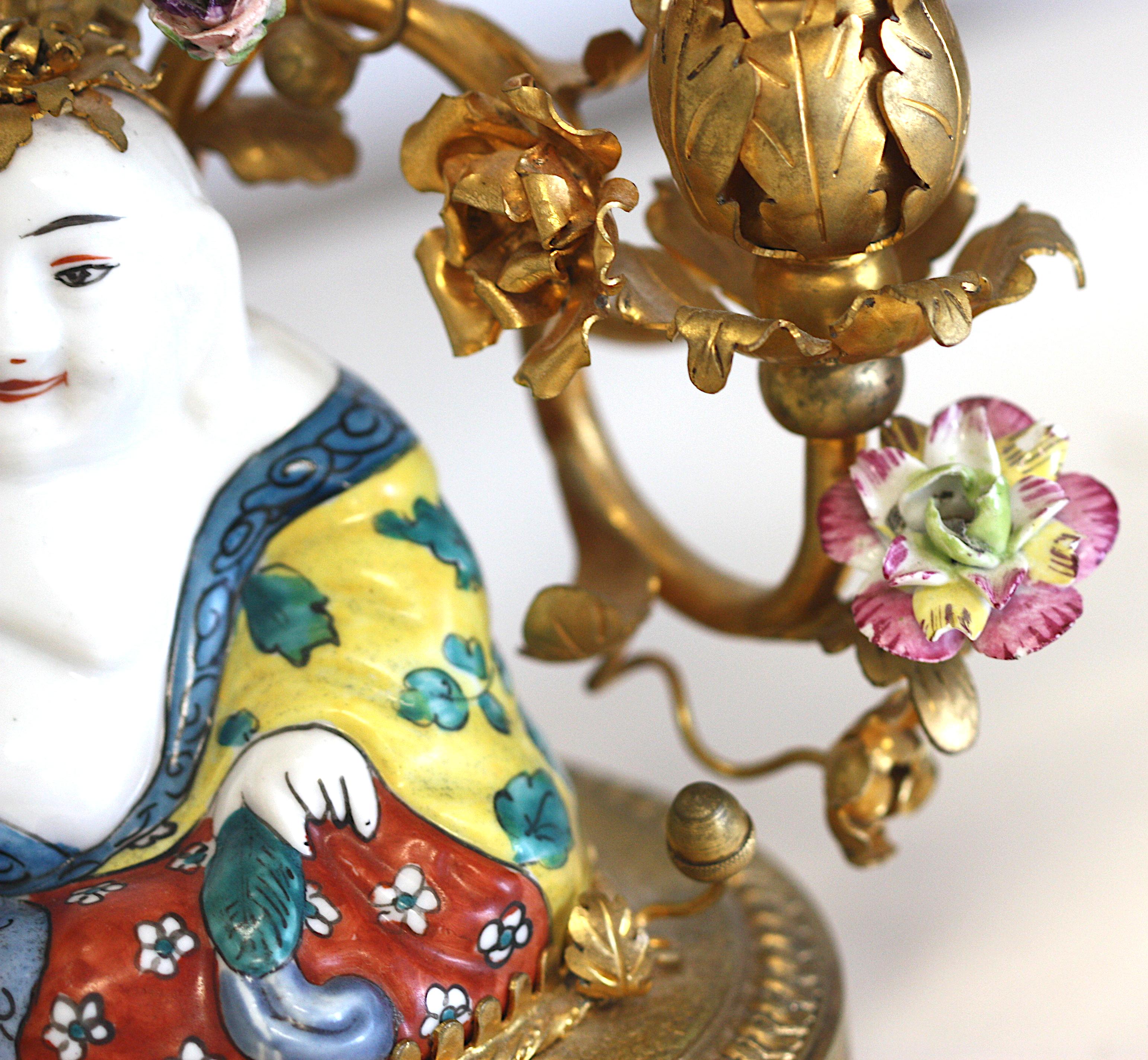 
Louis XV Style Porcelain Mtd. Gilt Bronze Two-Light Lamp
Composed of a porcelain seated Buddha, before two gilt bronze scrolling leafy candle arms, dotted with porcelain flowers, on an oval bronze base. 
Height overall, 23 in. (58.42 cm.), Width 11