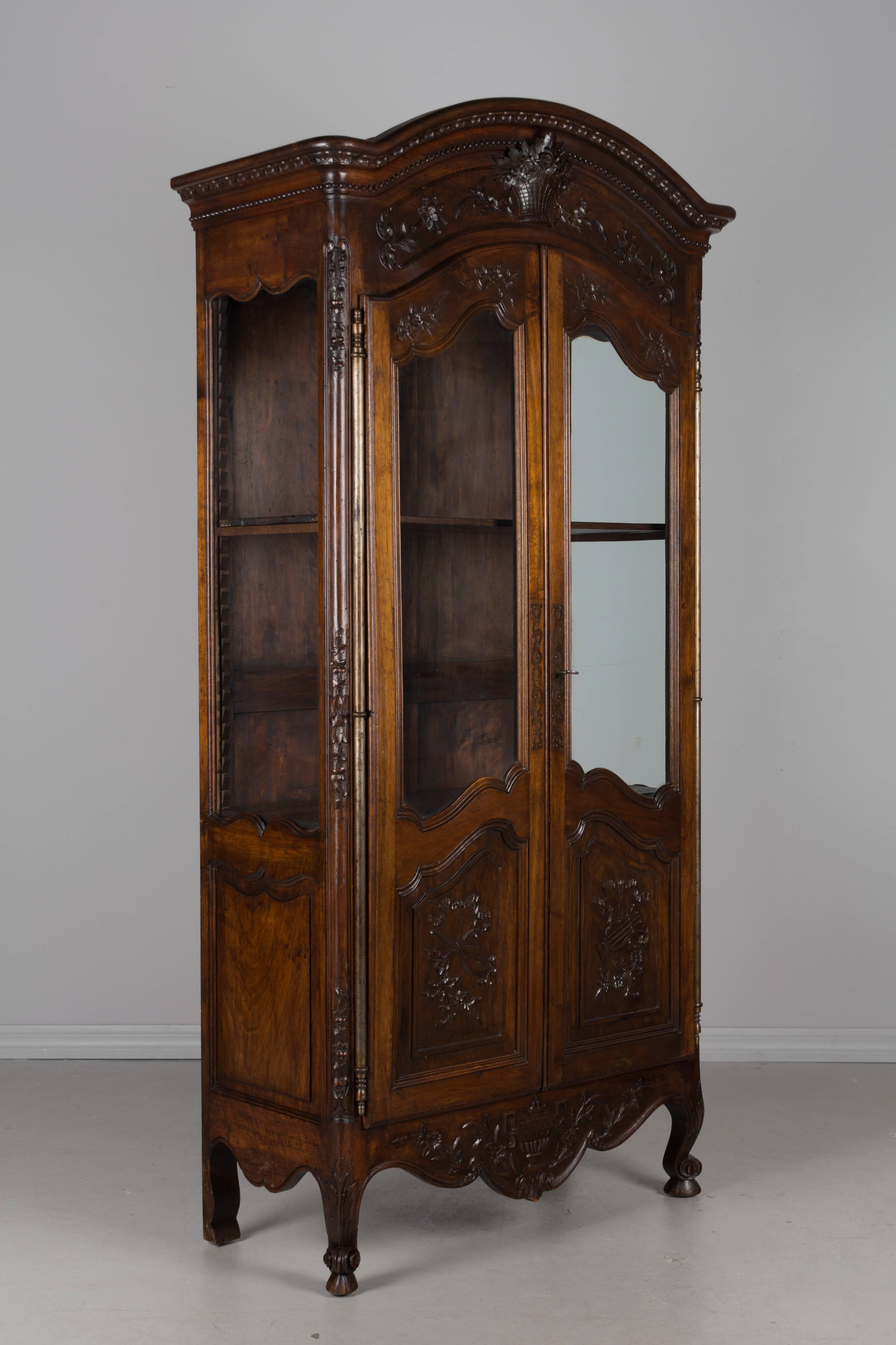An early 20th century French Louis XV style Provençal vitrine, or display cabinet. Made of walnut and with nice floral carvings including a flower basket below a chapeau de gendarme crown, lyres on the door panels and an urn carved in relief on the