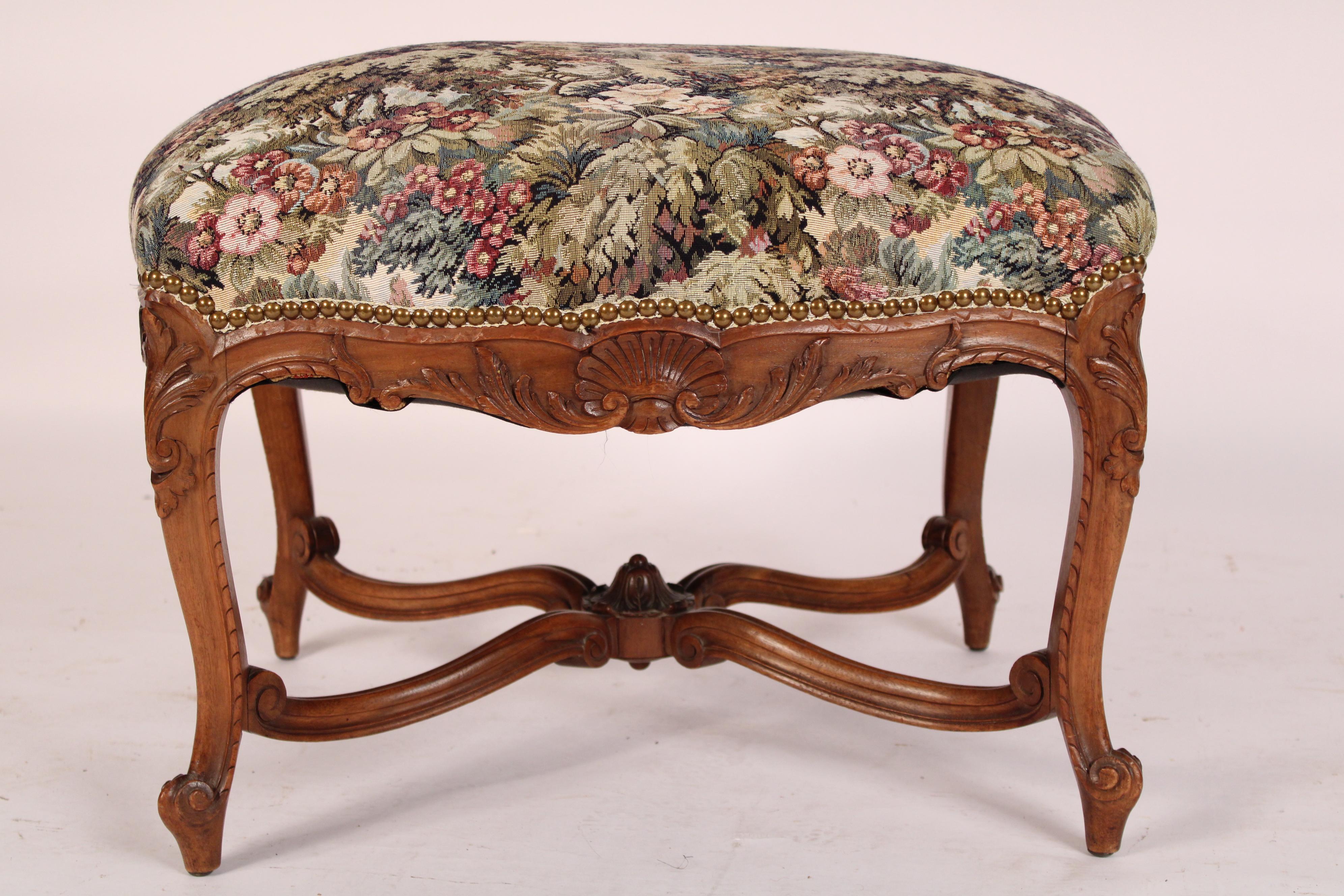 Antique Louis XV provincial style bench, circa 1920's. With a tapestry style seat with brass nail head trim, acanthus and shell carved seat rails, cabriole legs with acanthus carved knees and French fiddle feet, joined by X shaped stretcher bars.