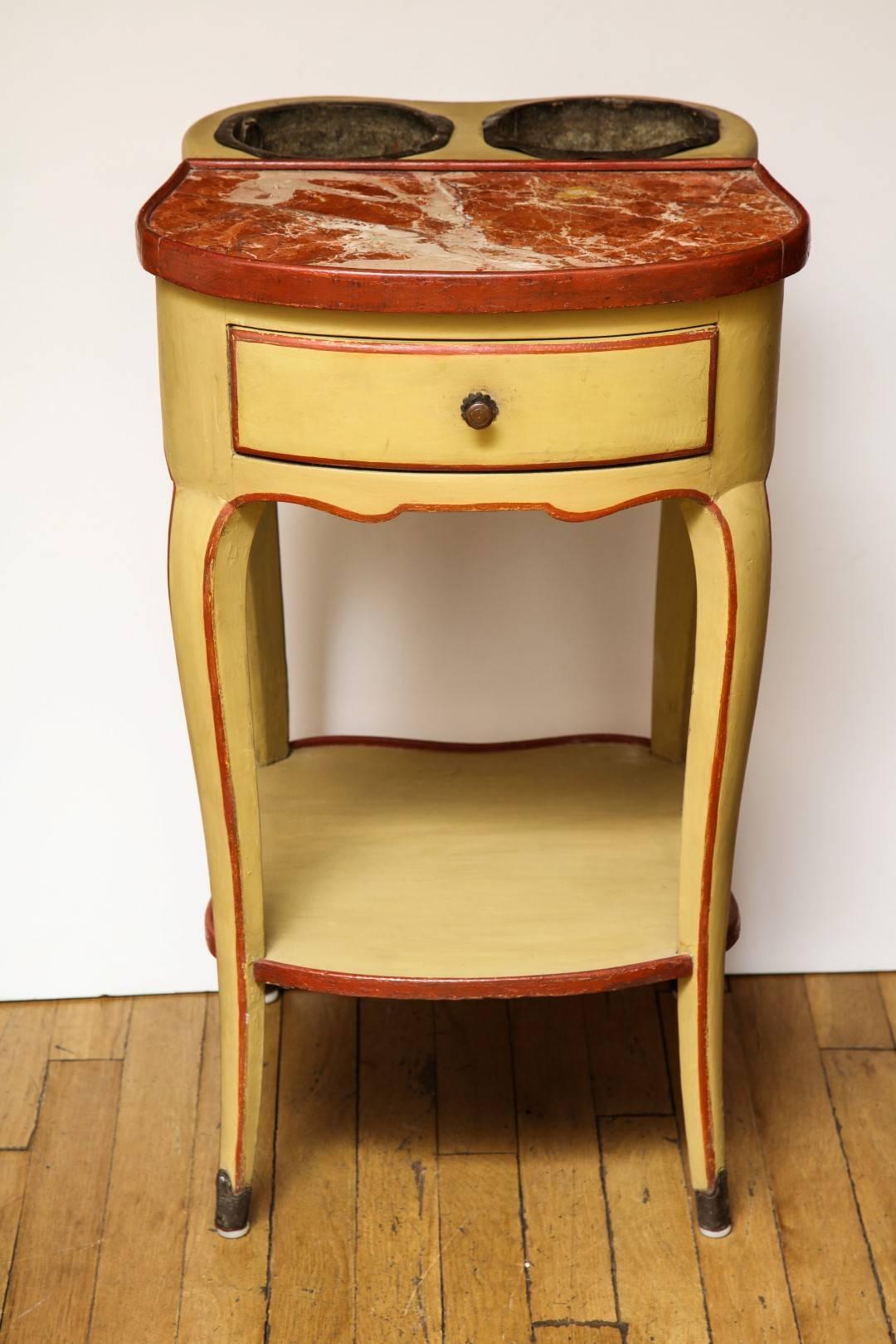 A Louis XV style rafraichissoir, the top fitted with a rouge marble tablet and two oval metal receptacles, above a scalloped apron with a drawer, the four slight cabriole legs terminating in sabots and joined by an under-tier, circa 1890. The