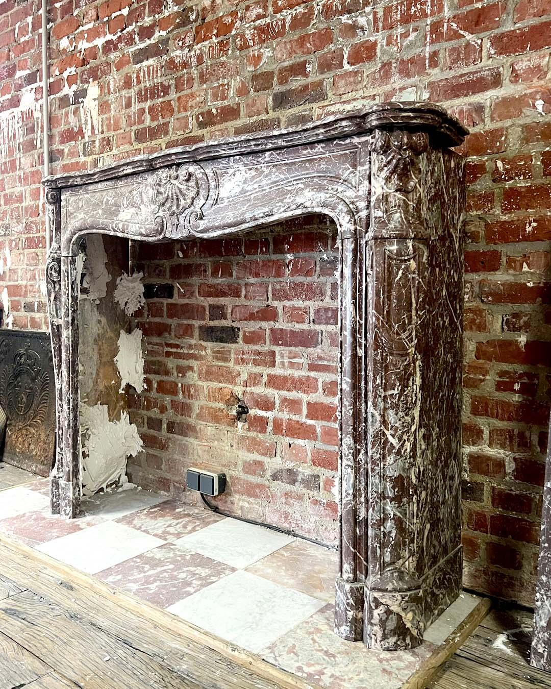 Elegant Louis XV style fireplace crafted from richly veined red marble, dating from the 19th century. This refined piece features the graceful, asymmetrical curves and delicate ornamentation characteristic of the Rococo period.

The serpentine front