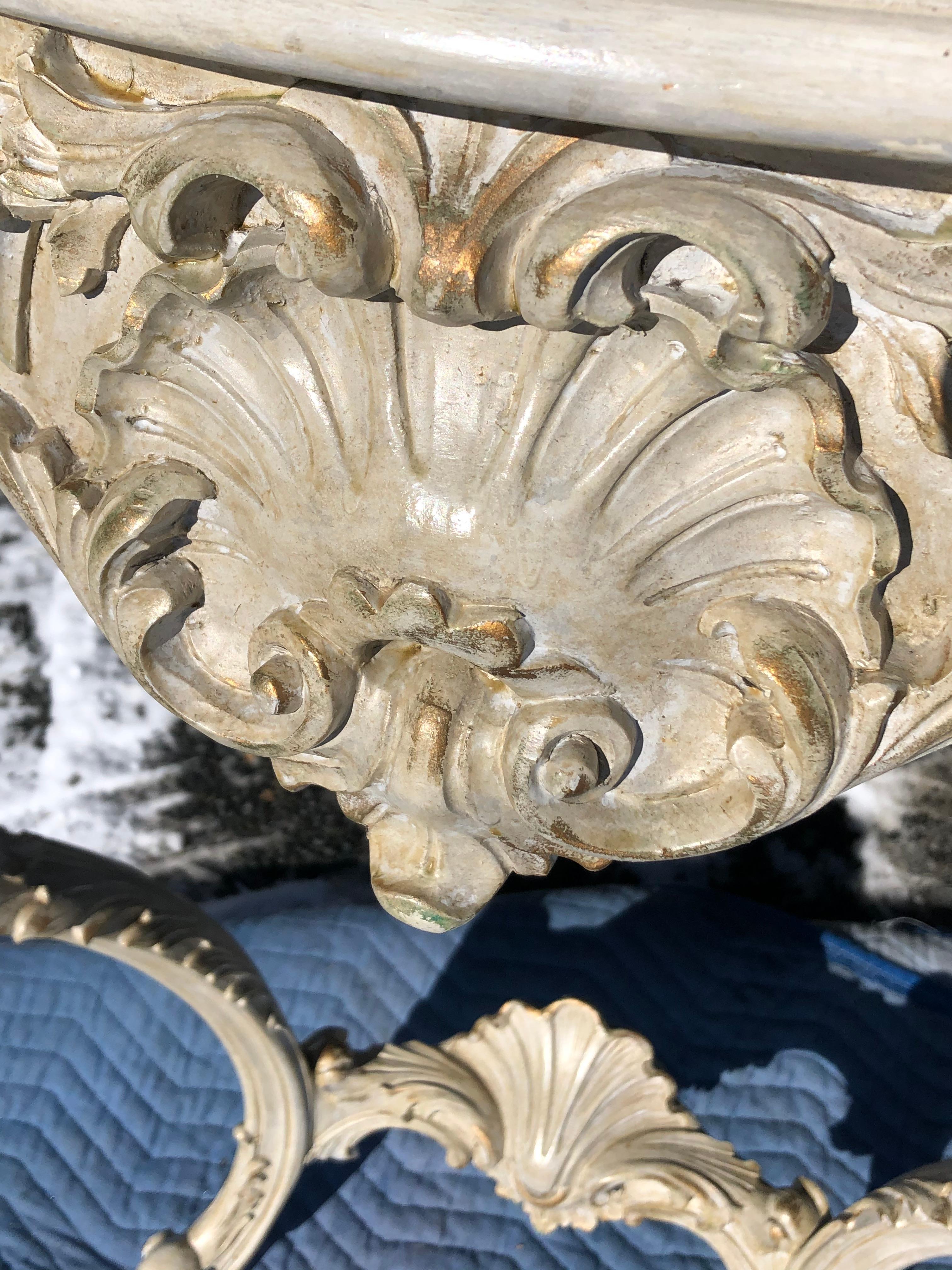 A gorgeous ivory painted parcel-gilt carved wood console table having an overhanging serpentine top above a front frieze with shell and foliate motifs, a shell carved stretcher connecting the pair of foliate carved cabriole legs.
Needs to be