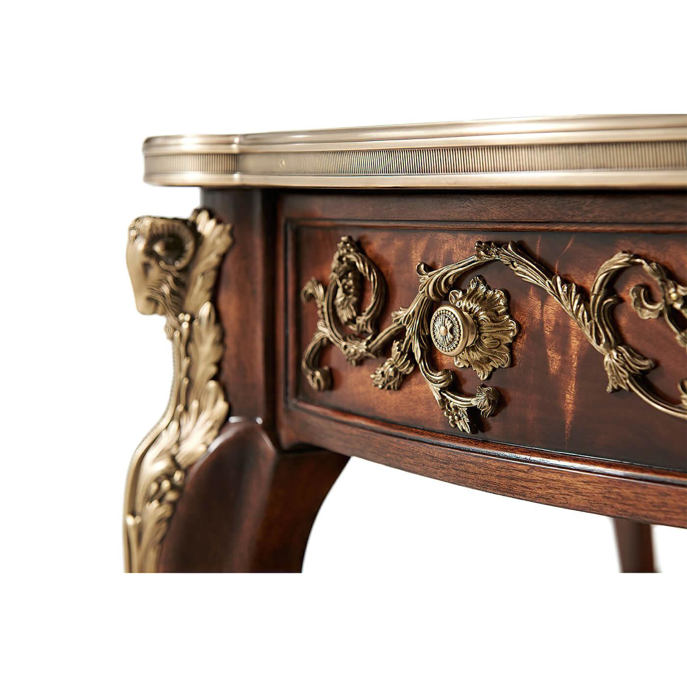 A French Louis XV style mahogany cross-banded banded cocktail table applied with very fine brass mounts, the brass bound circular top with protruding corners, the frieze with two opposing drawers, on ram's head capital cabriole legs joined by an