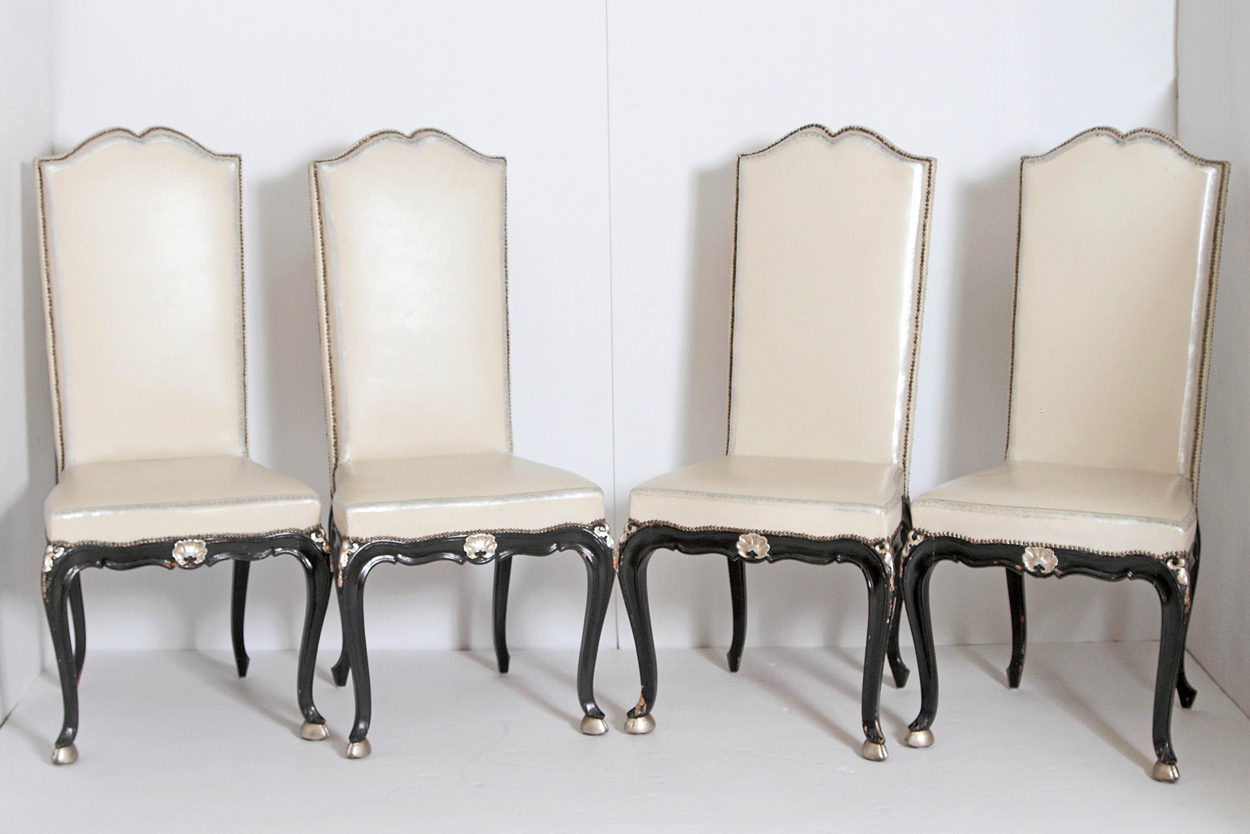 A set of twelve high back dining side chairs Louis XV style with ebonized wood frames with gilt bronze mounts at knees and gilt shell centre front. Gilt hoof feet. Cream leather upholstery with nail-heads.